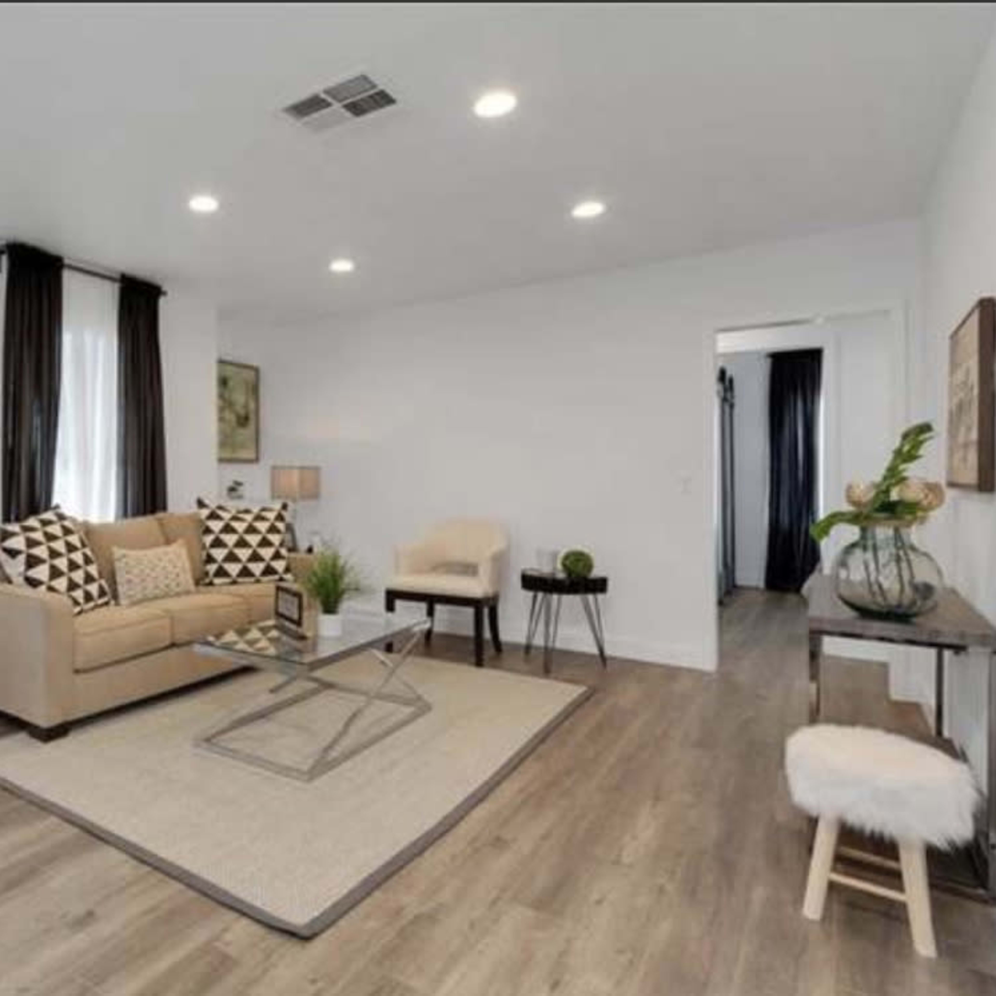 The living room features a neutral-colored sofa with patterned cushions, a coffee table on a large area rug, and a set of minimalist decor elements.