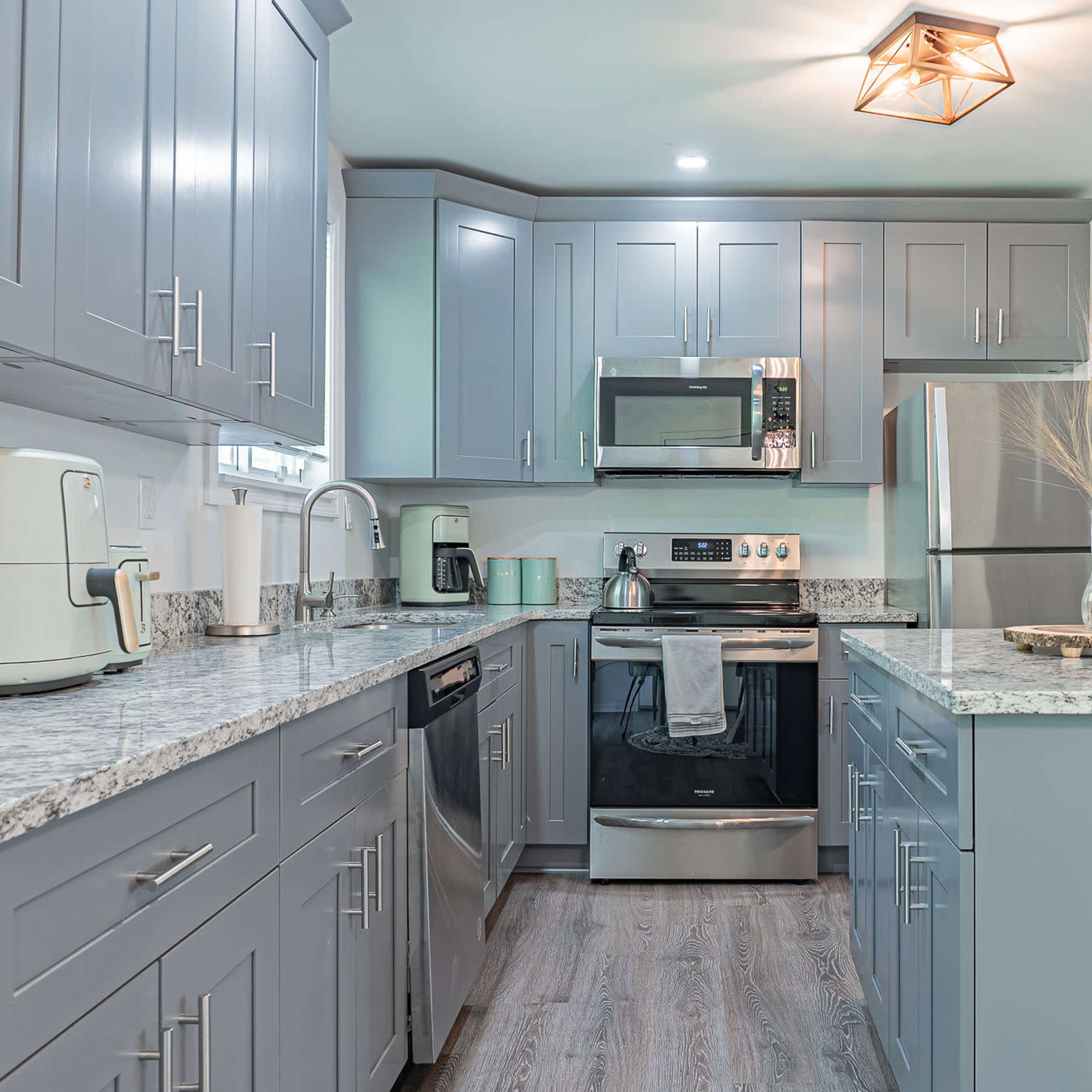 A modern kitchen with gray cabinets, a stainless steel refrigerator, and granite countertops.
