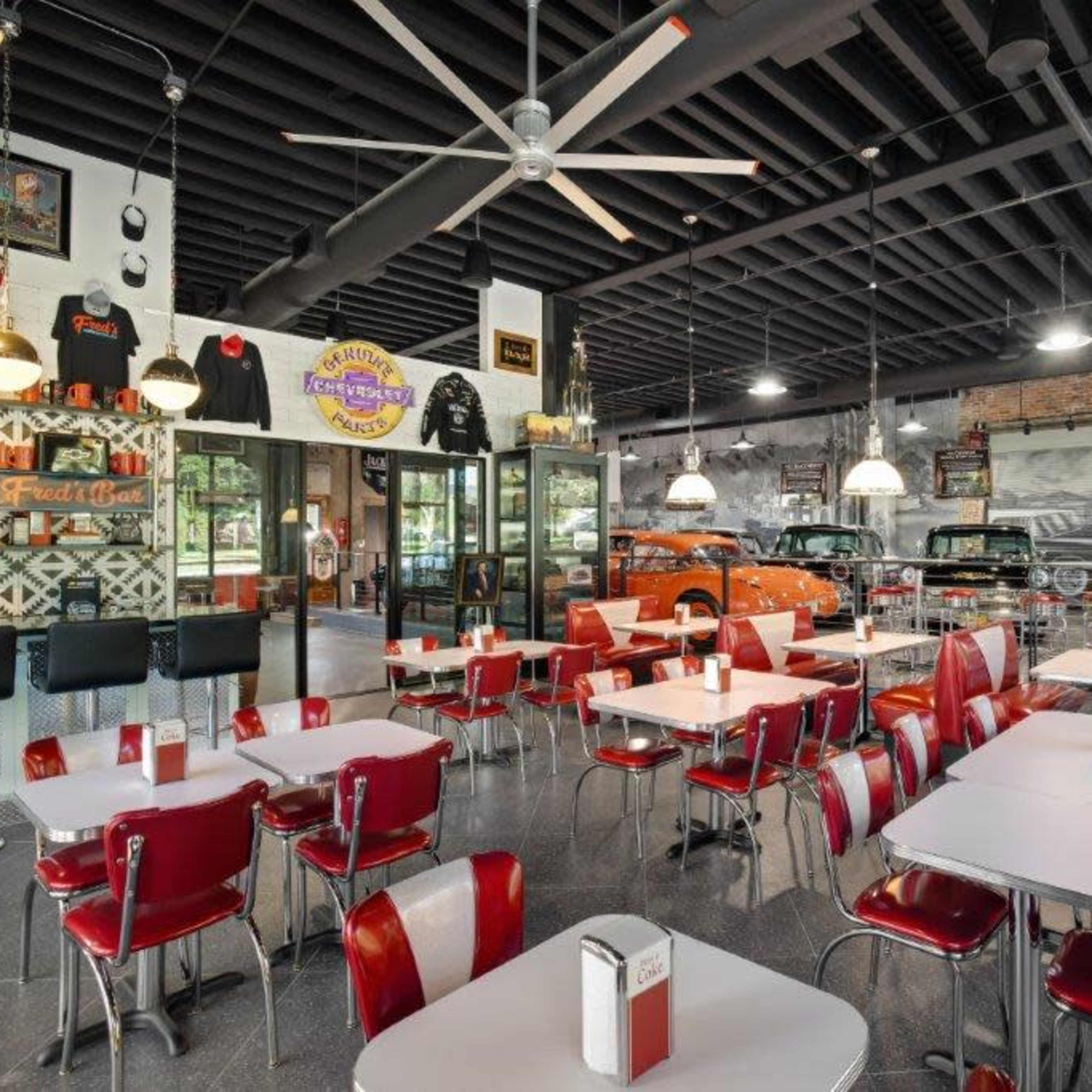 The scene shows a retro diner with red and white seating, a counter area, and vintage cars displayed in the background.