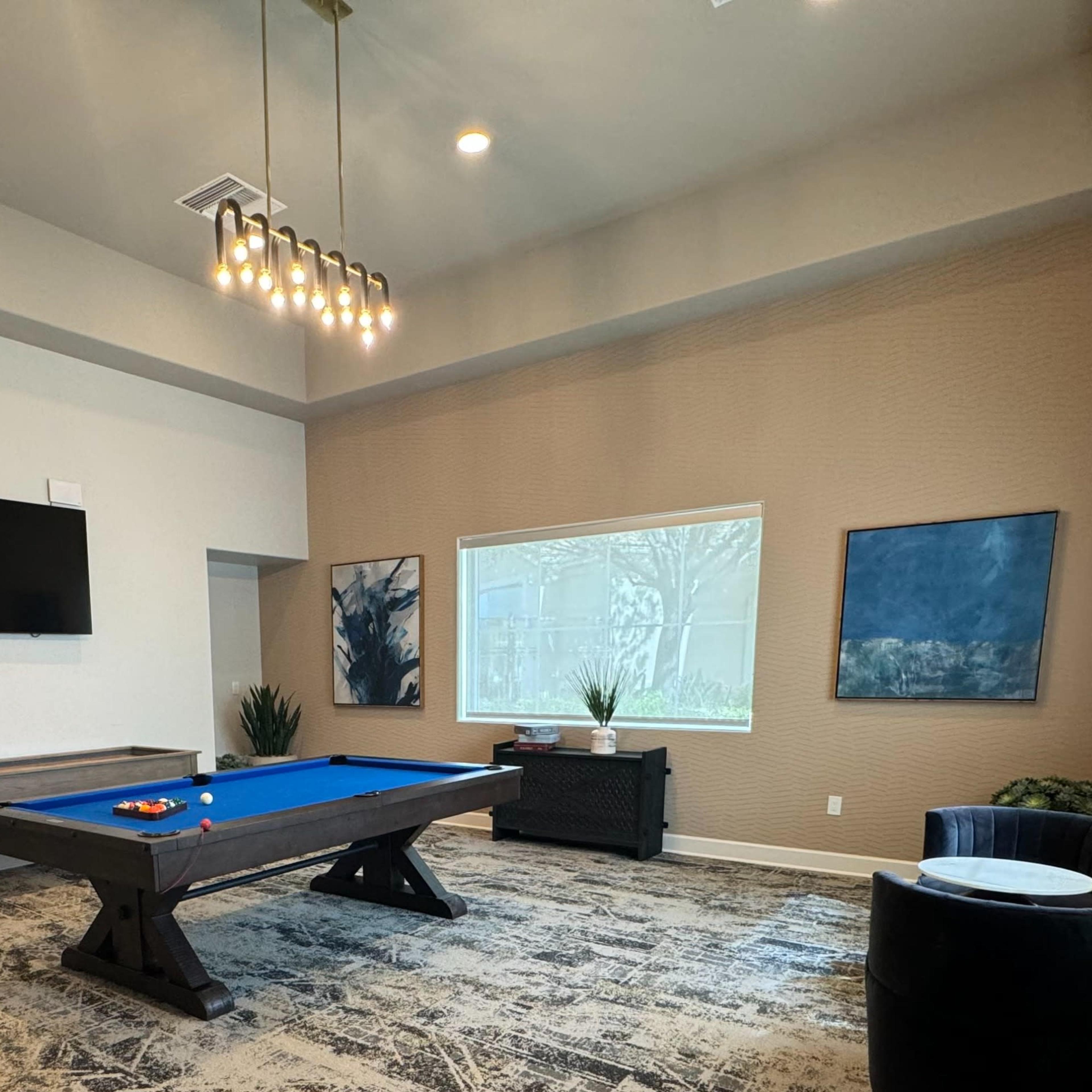 The room features a pool table, a television mounted on the wall, and two artworks displayed near a large window.