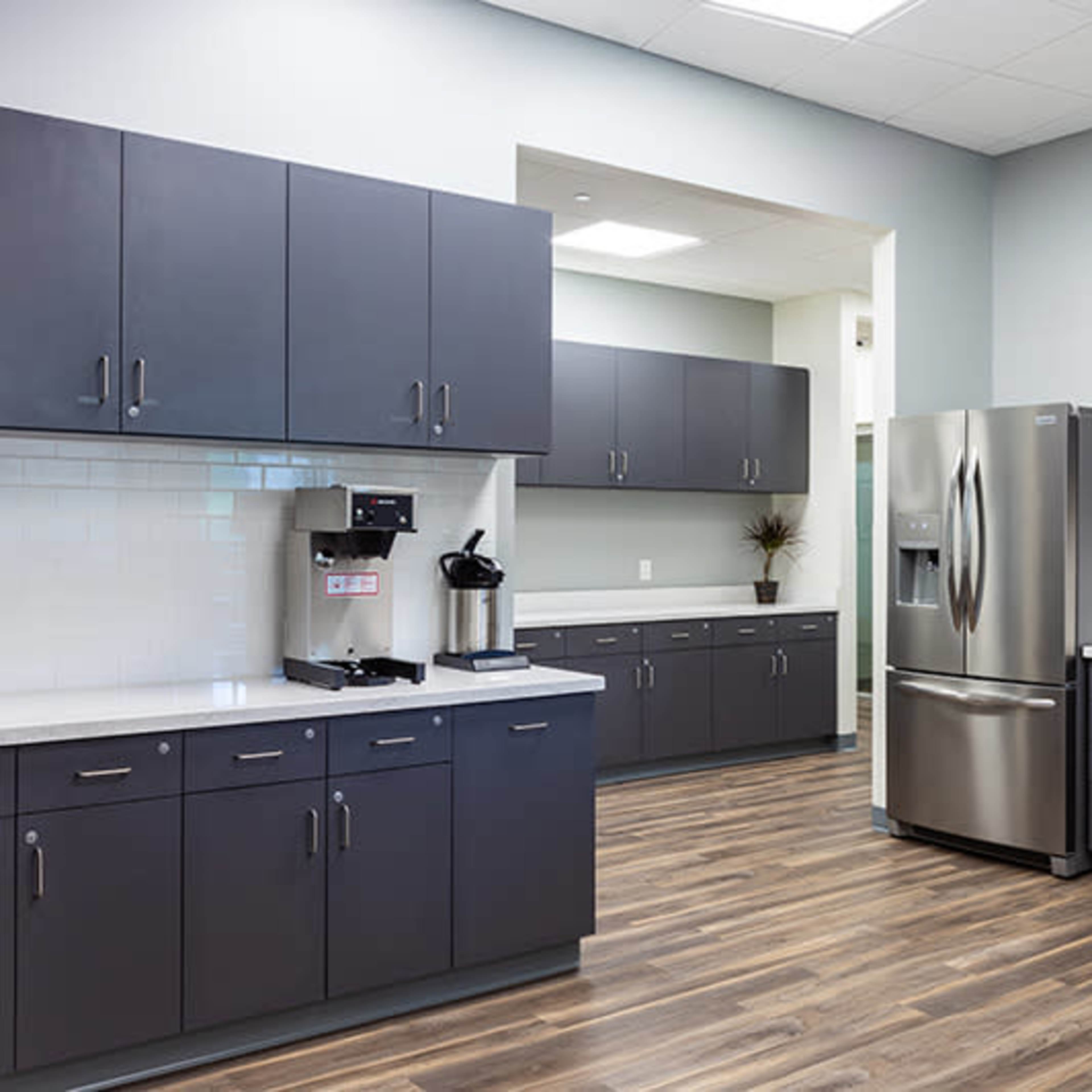 A modern kitchen with gray cabinets, a stainless steel refrigerator, and a coffee station.