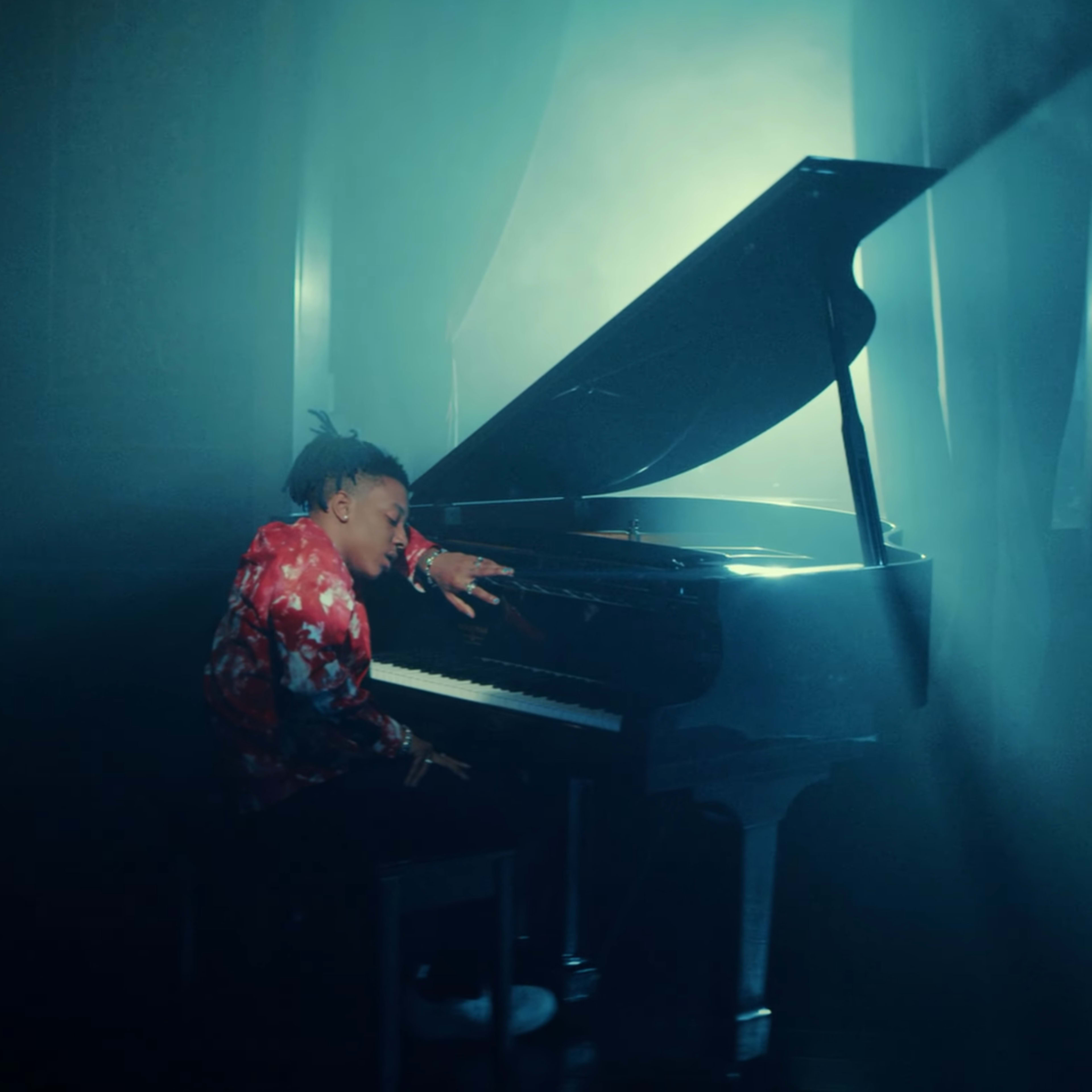 A musician plays a grand piano in a dimly lit room with dramatic lighting and a haze of smoke.