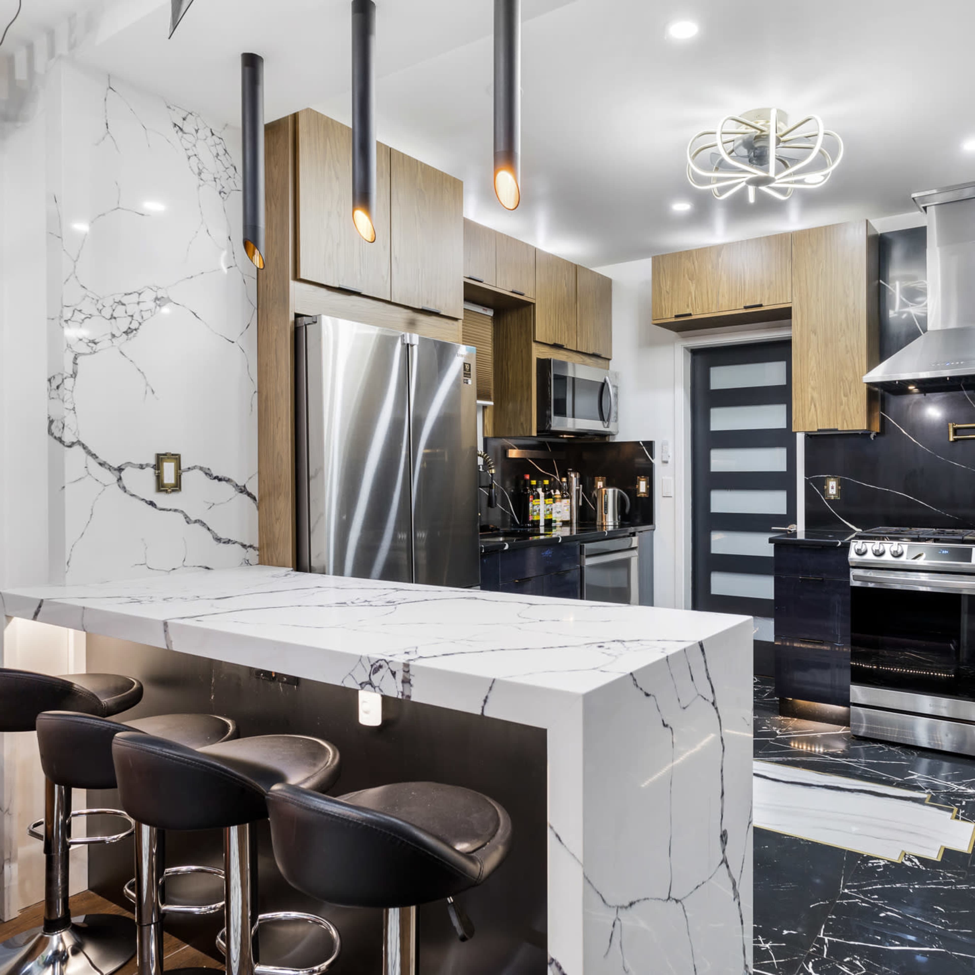 The kitchen features marble countertops, wooden cabinetry, and modern stainless steel appliances with a central island and bar seating.