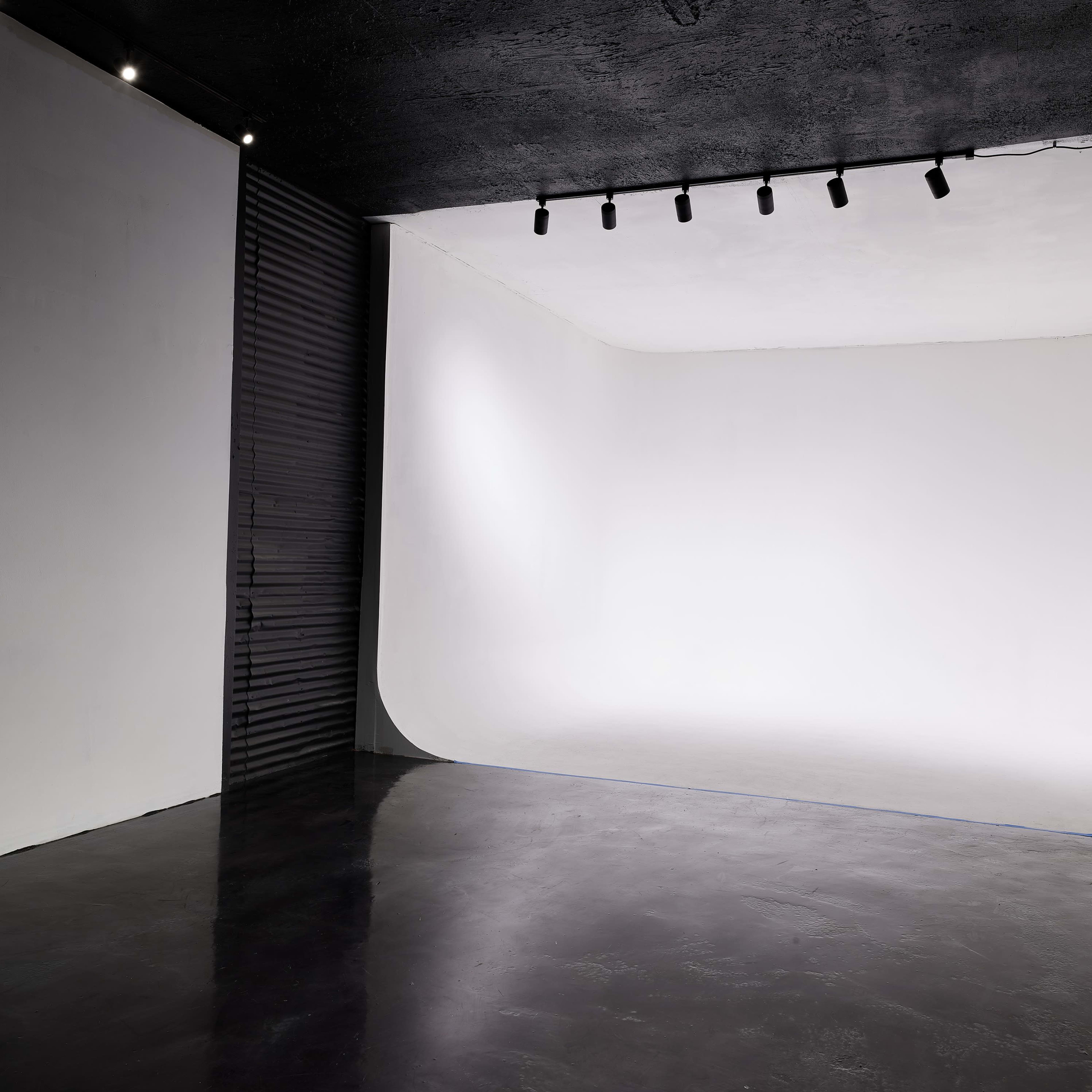 A minimalist photography studio with a curved white backdrop and dark flooring.