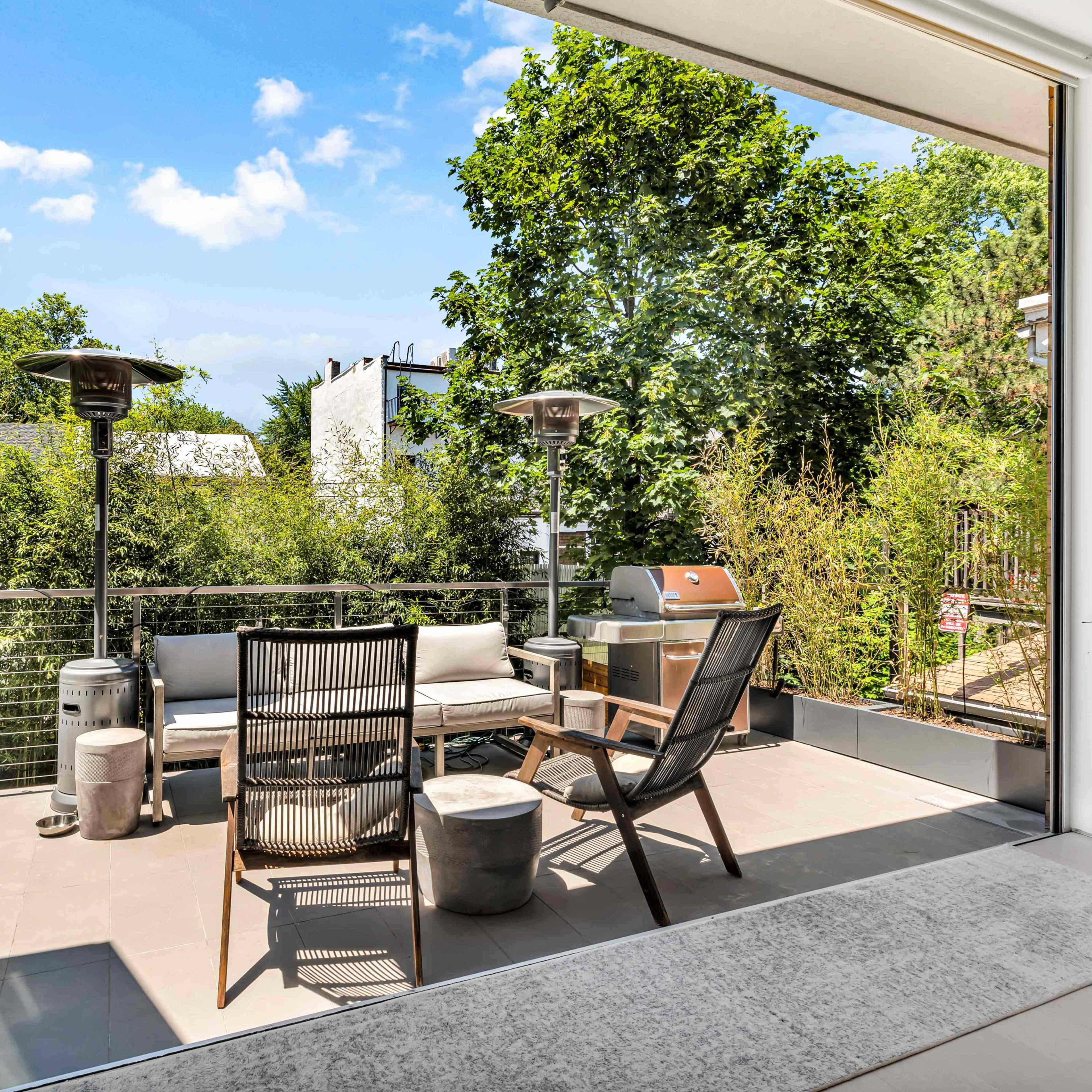 A modern patio with outdoor seating and a grill overlooks a lush garden.