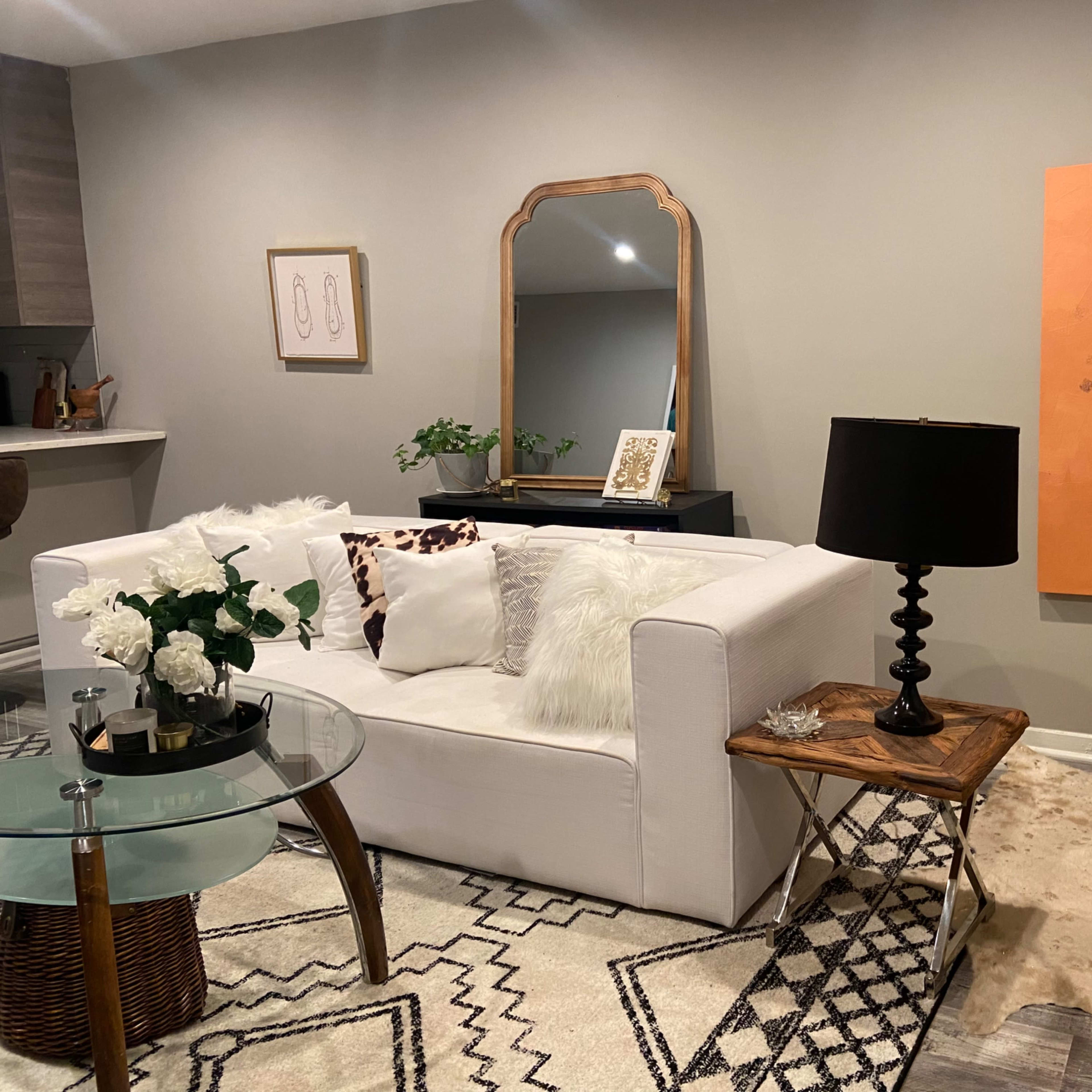 A modern living room with a white sofa, a glass coffee table, and an orange artwork of a raised fist on the wall.