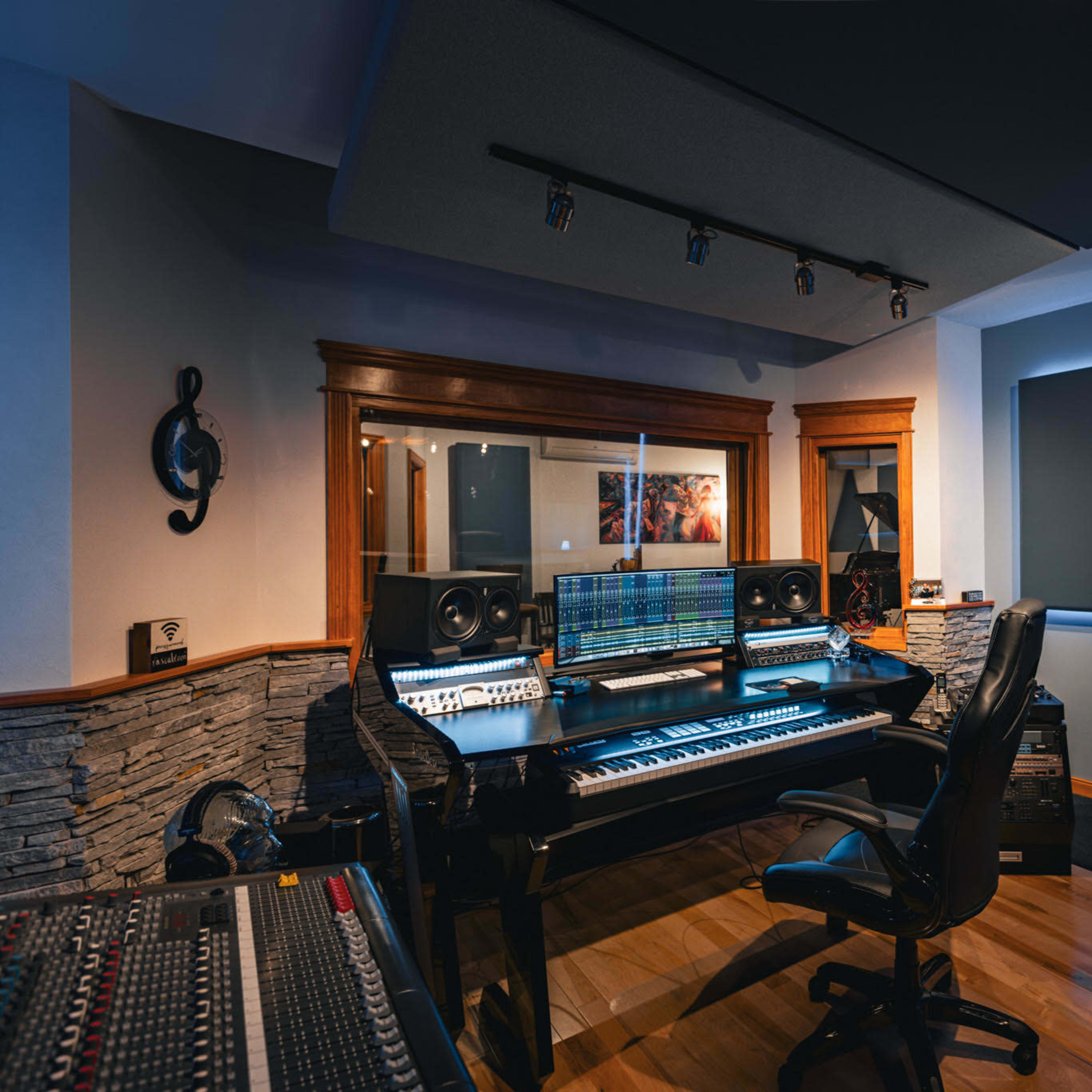 A modern recording studio with a central black piano keyboard, large speakers, and a computer setup, surrounded by wooden accents and acoustic panels.