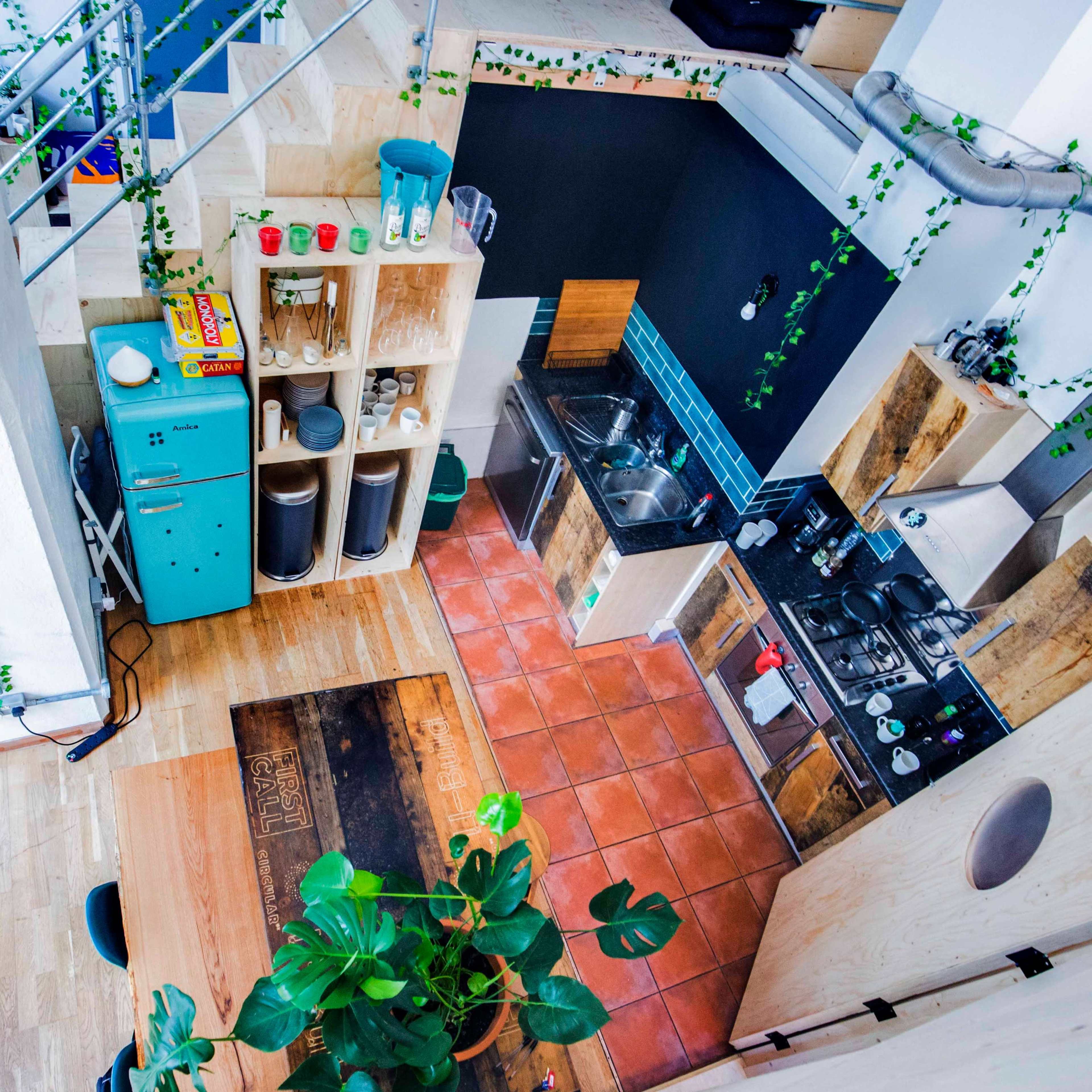 A modern kitchen with wooden cabinets, blue accents, a gas stove, and indoor plants, viewed from above.