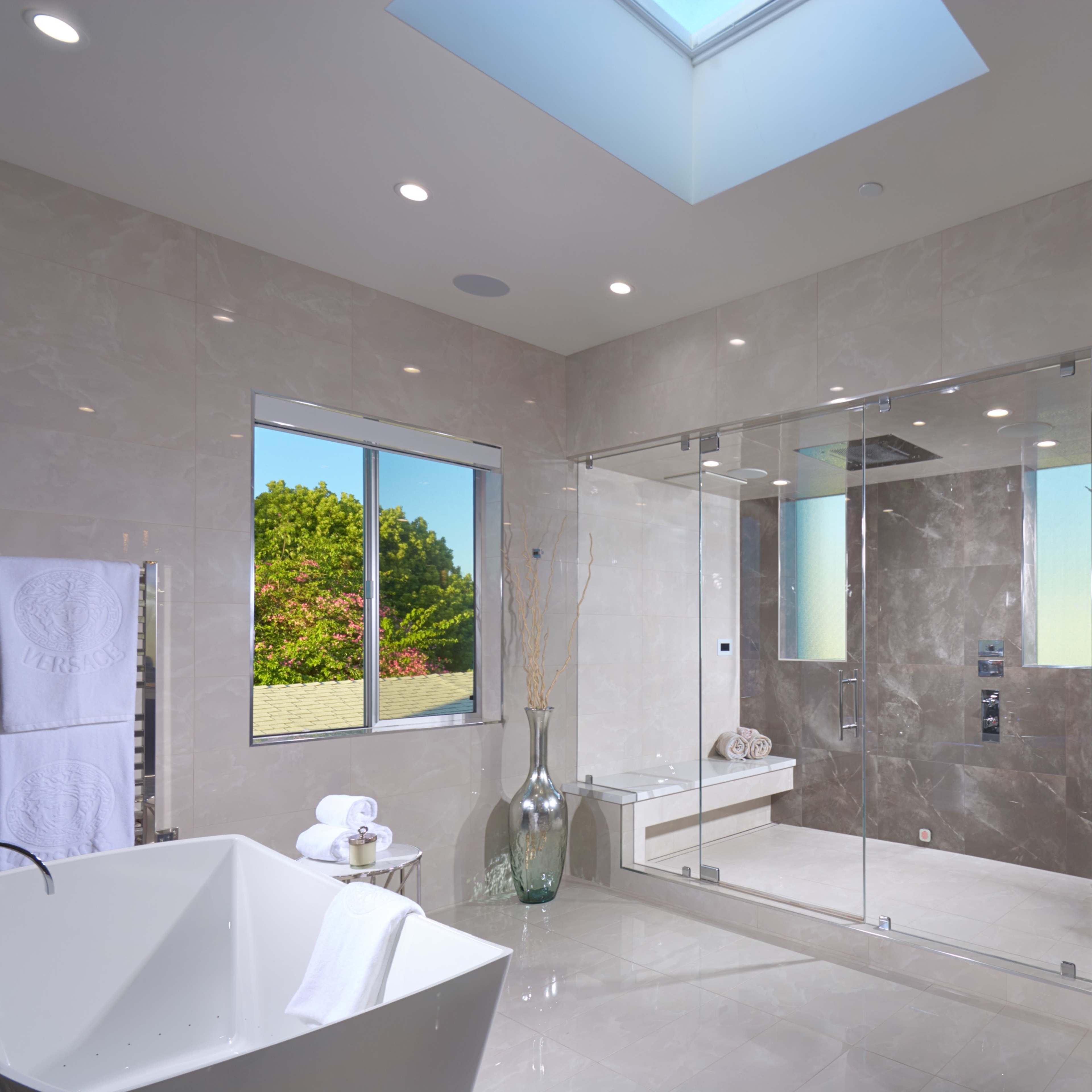 A modern bathroom featuring a glass-enclosed shower, a freestanding bathtub, and a skylight allowing natural light to enter the space.