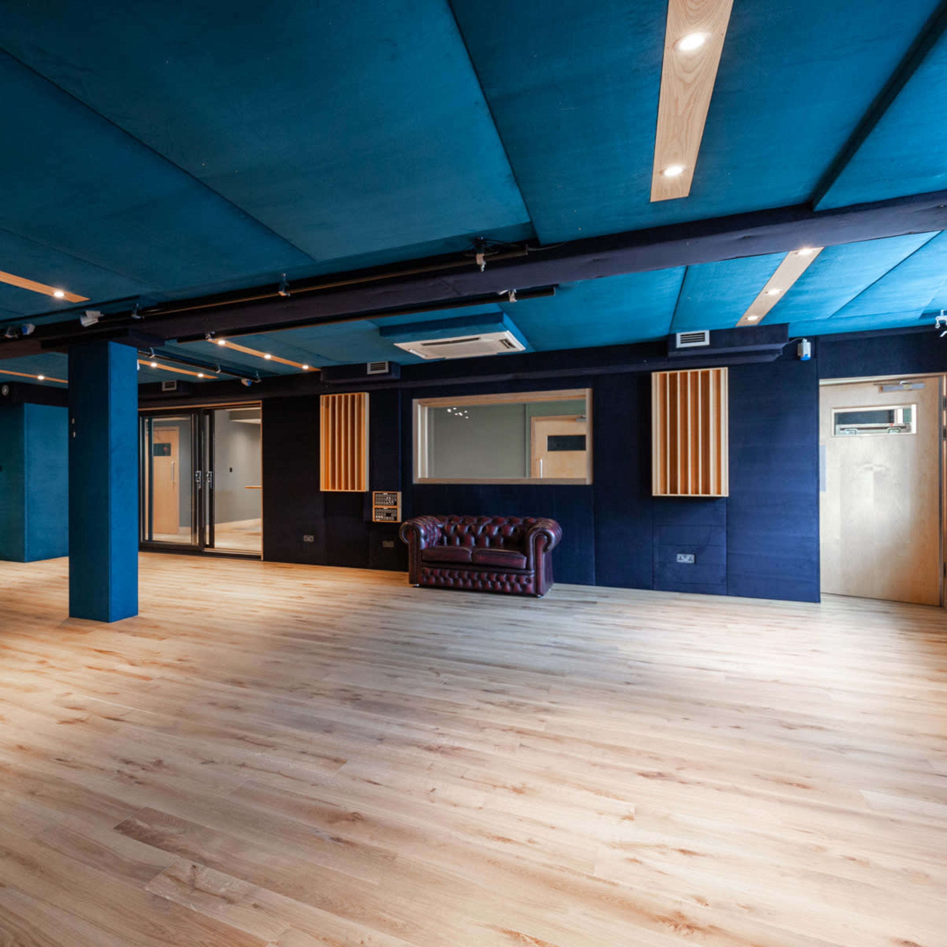 A spacious room with dark blue walls and a wooden floor, featuring two leather sofas and doors on the sides.