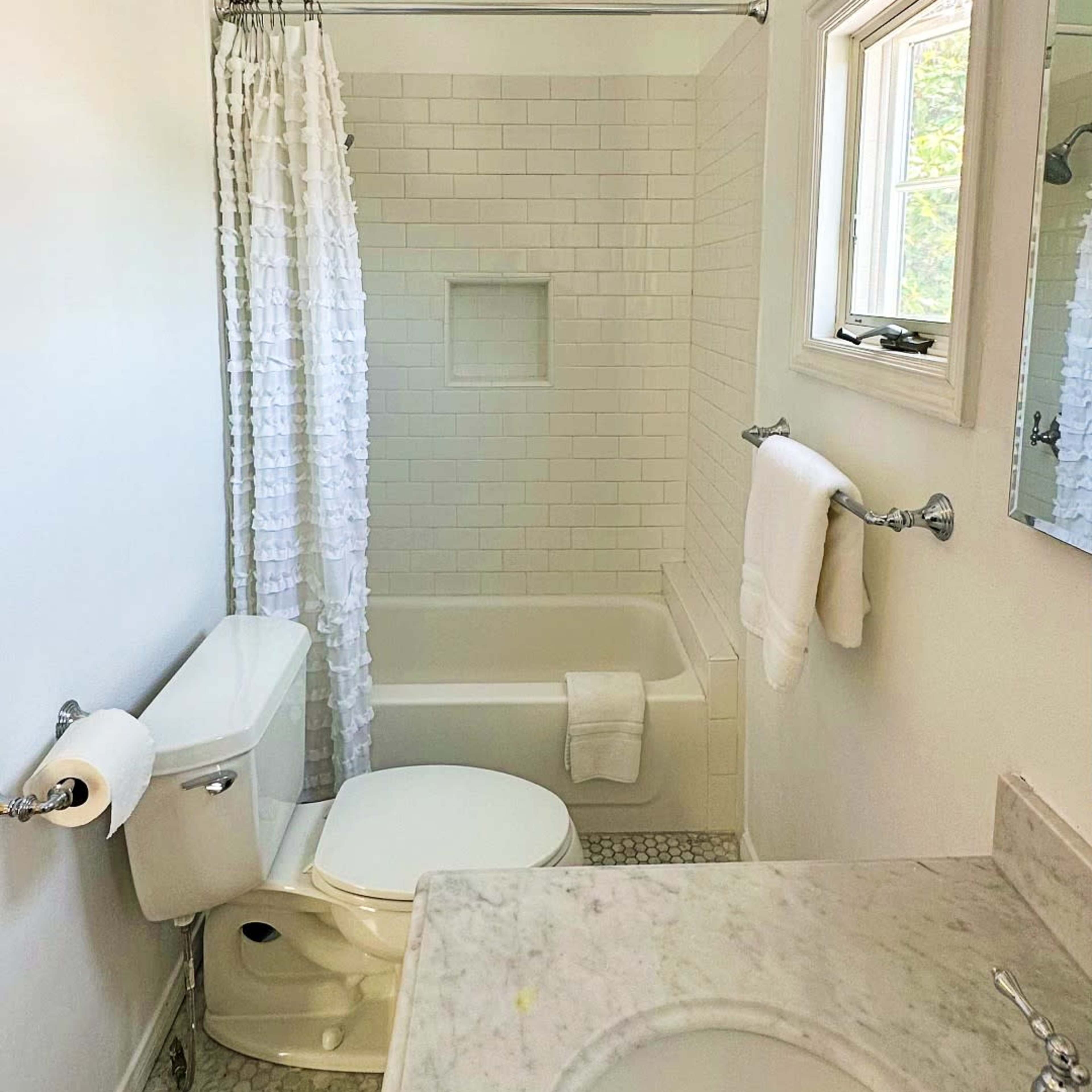 The bathroom features a white tiled shower area, a bathtub, a toilet, and a marble countertop with a sink.