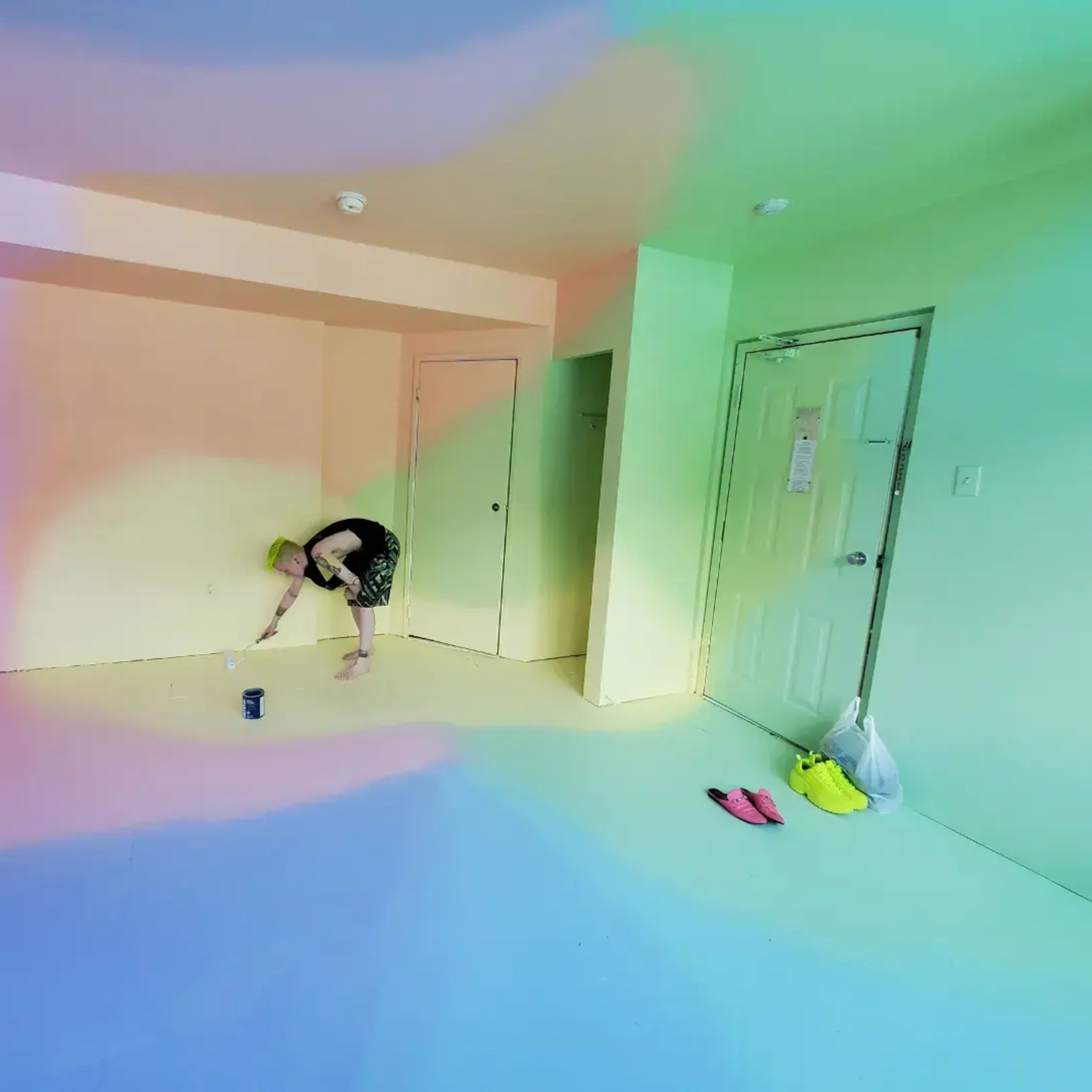 A person is painting the walls of a brightly colored room with gradient shades of pastel hues.