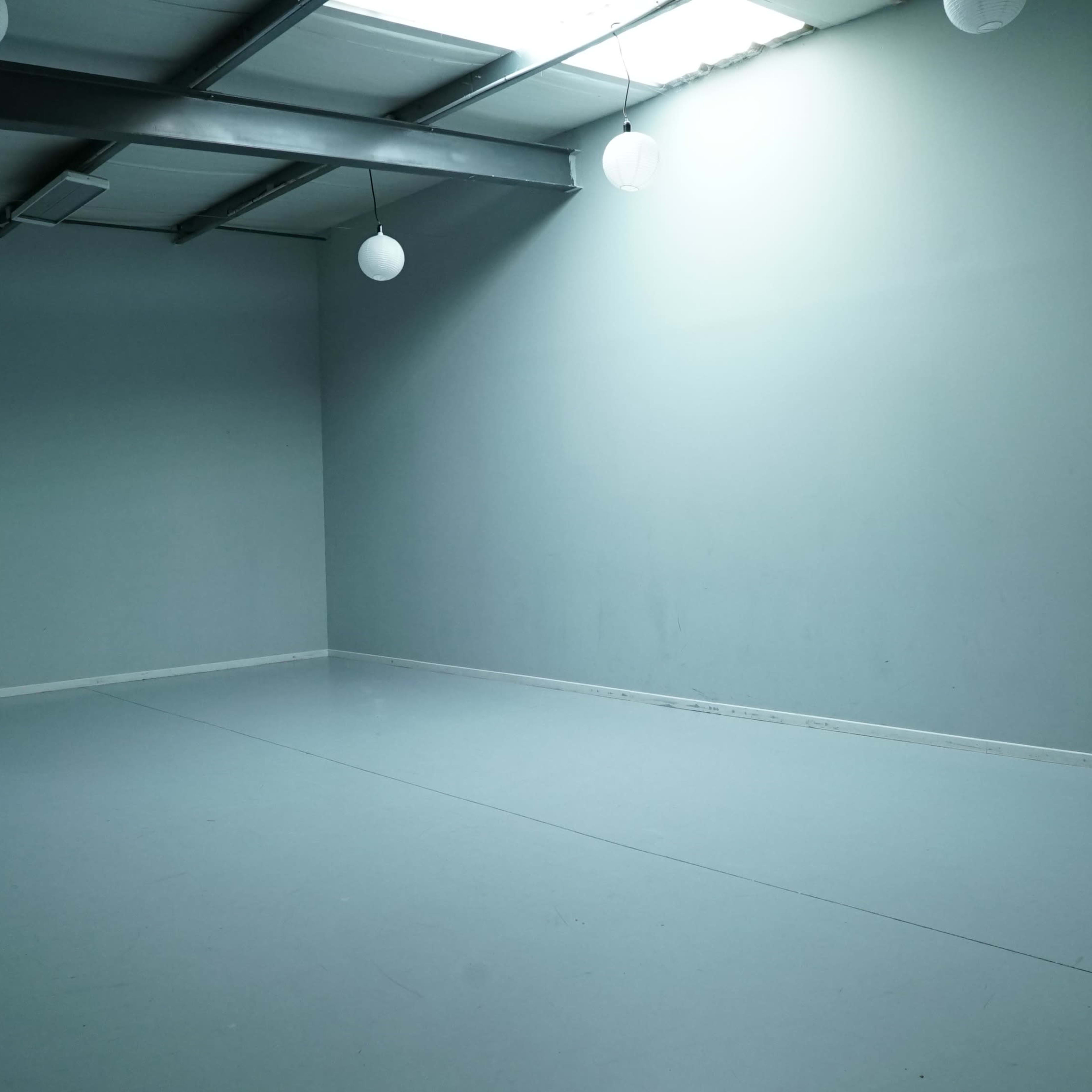 An empty room with a gray wall, concrete floor, and overhead light fixtures.