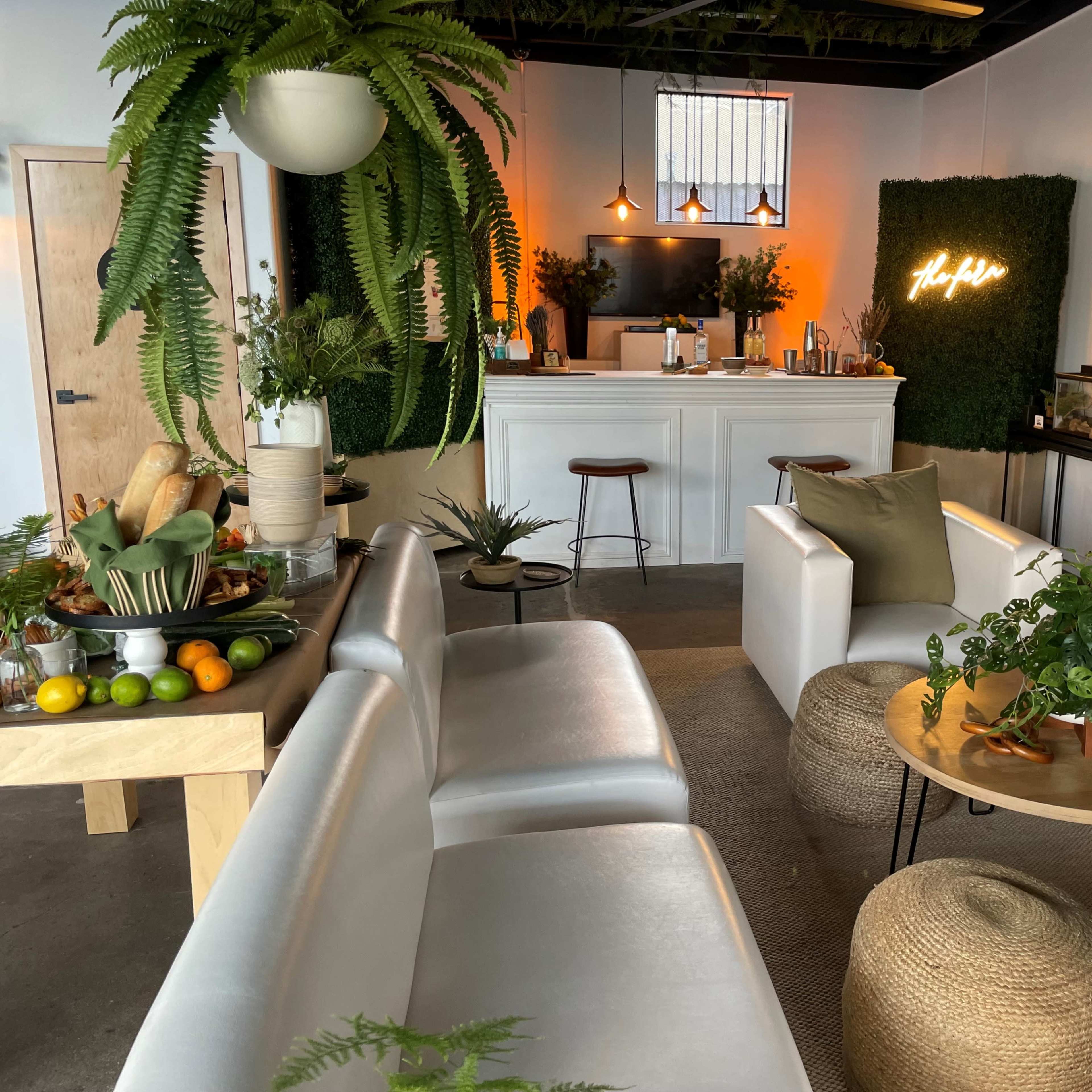 A modern interior space featuring white furniture, greenery, and a minimalist bar area.