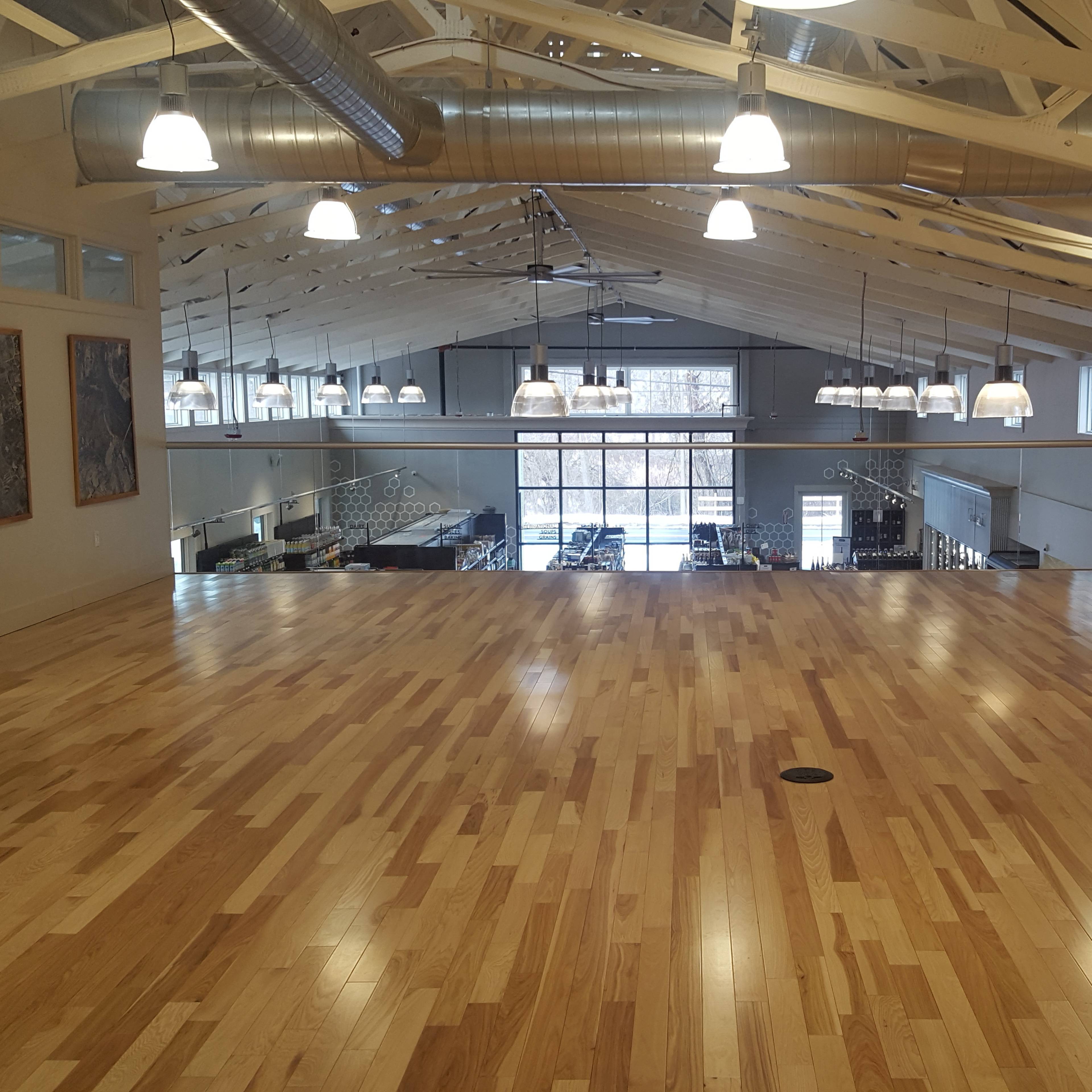 A spacious wooden floor area with large windows and industrial-style lighting in a building with exposed beams.