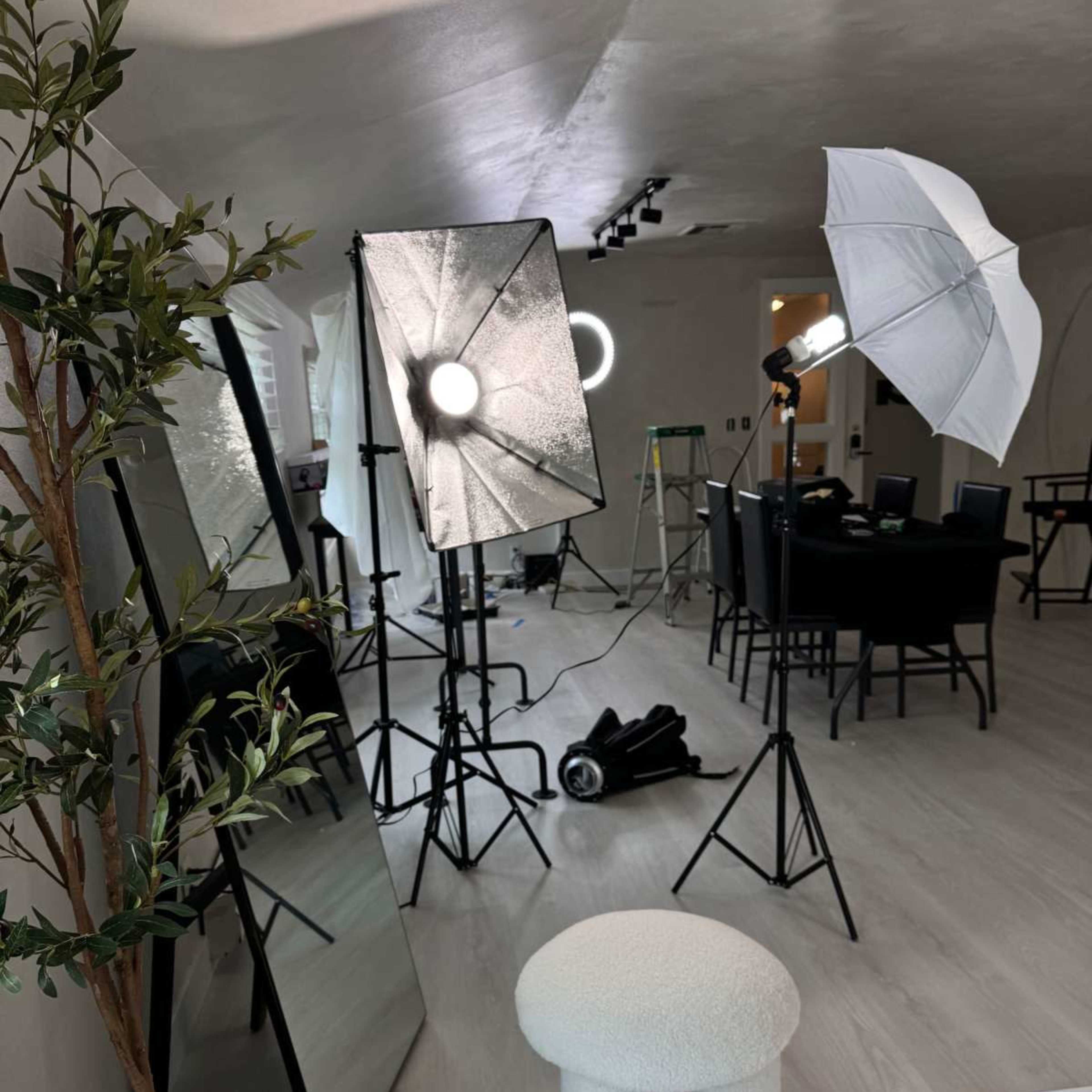 A bright indoor studio setup with lighting equipment, a mirror, and furniture arranged for a photoshoot.