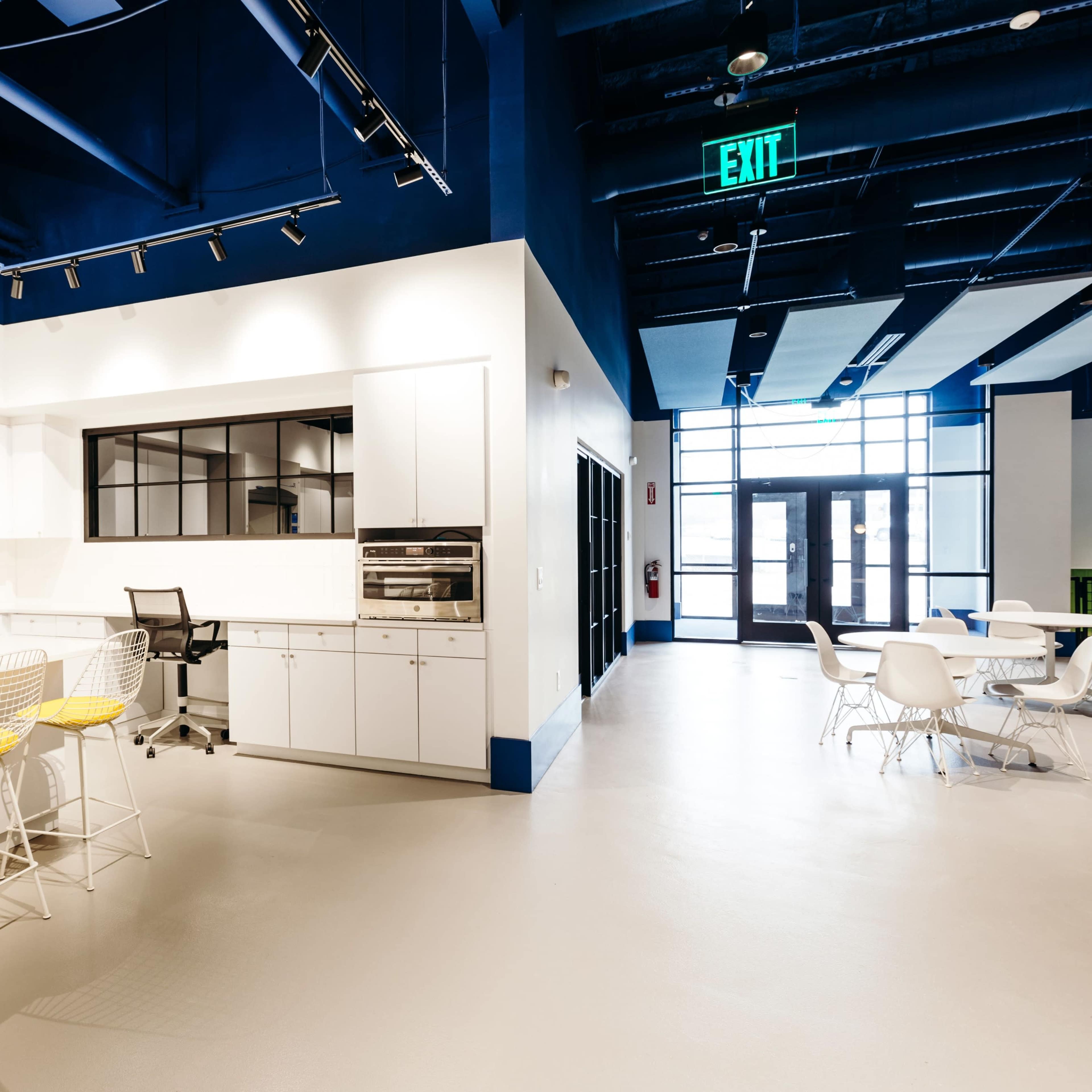 A modern kitchen and dining area with white cabinetry, yellow bar stools at the counter, and a table with white chairs.