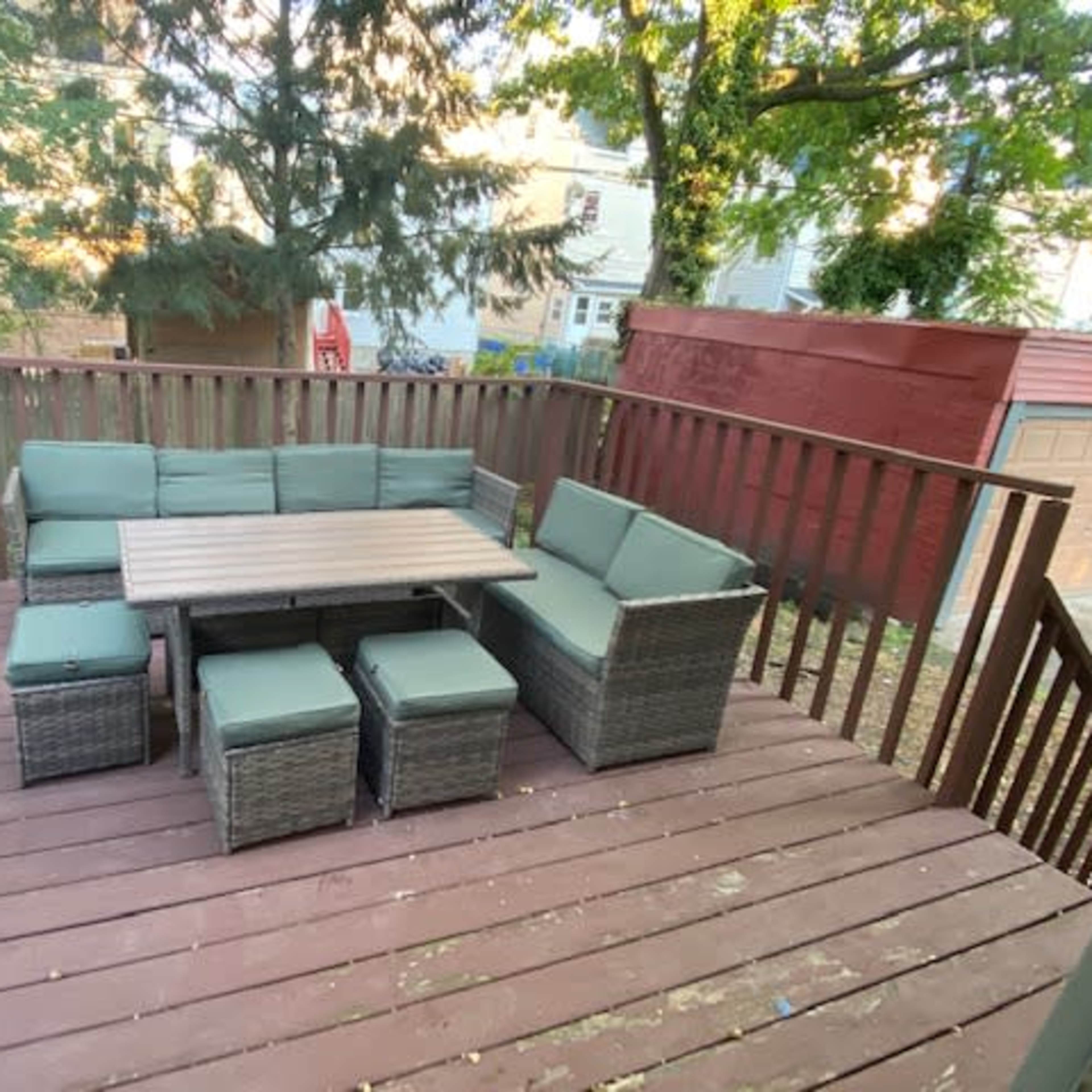 A deck features a seating arrangement with a table and cushions, surrounded by trees and houses in the background.
