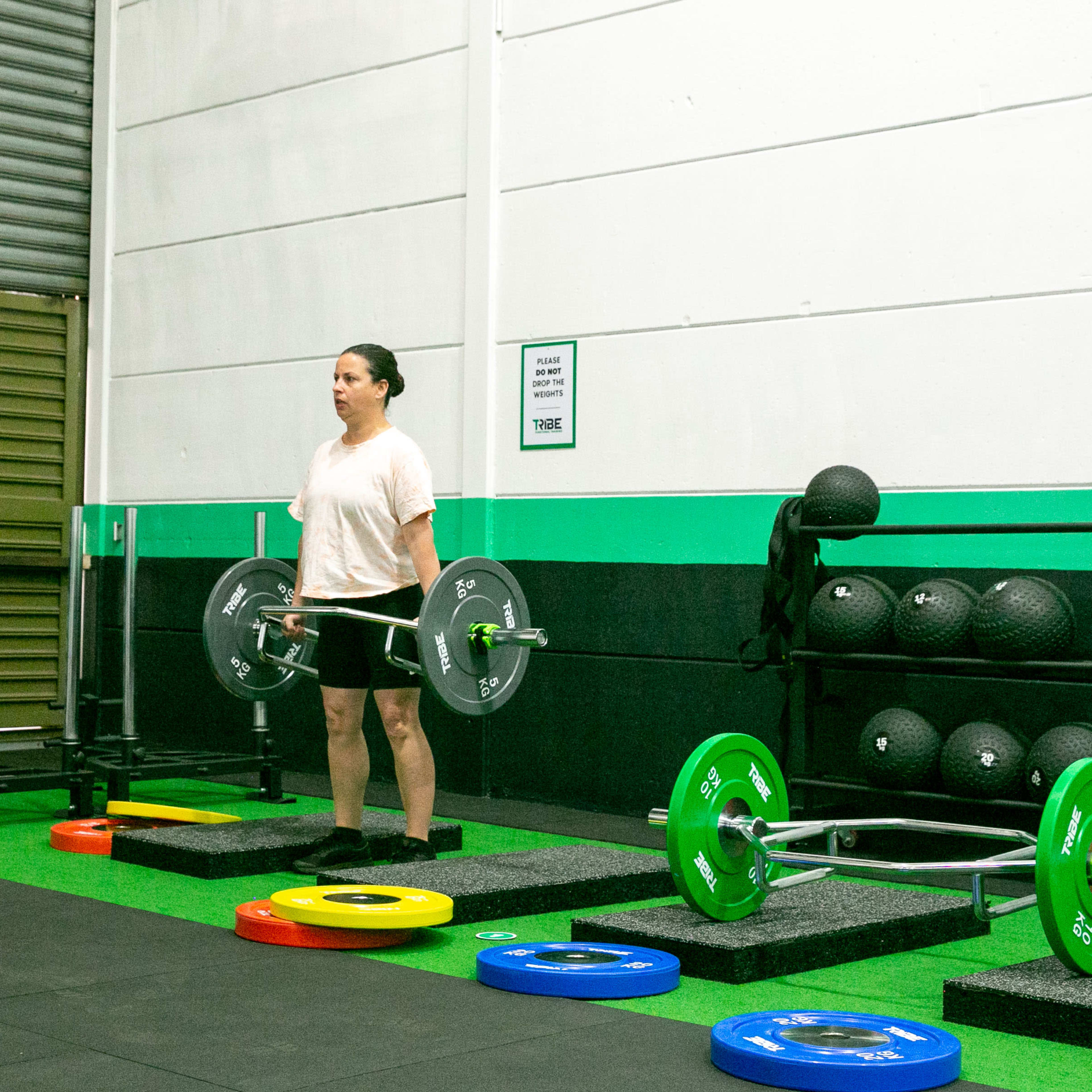 A person stands with a barbell in a gym, next to colorful weight plates and fitness equipment.