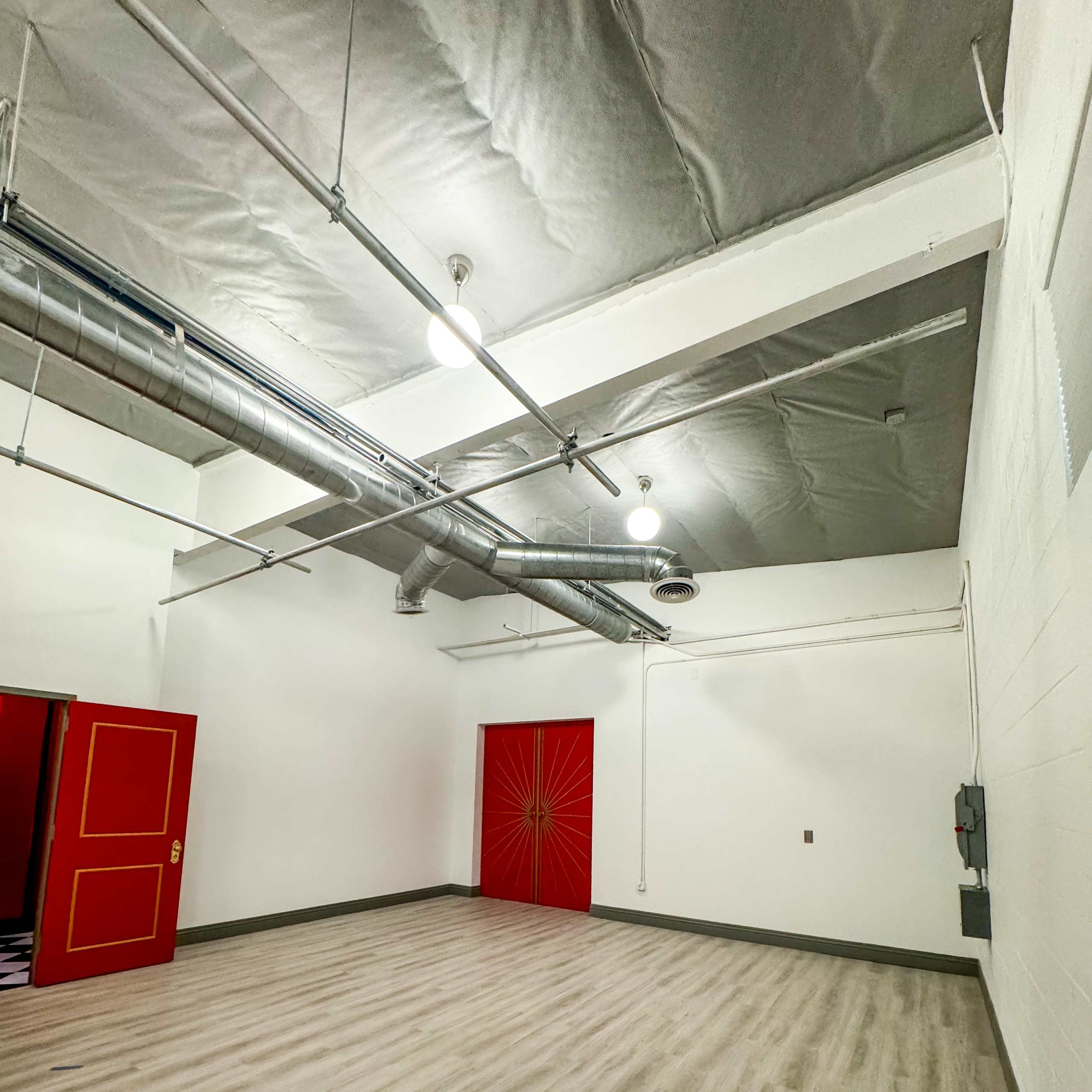 An empty room with a wooden floor, white walls, and a red door featuring a sunburst design.