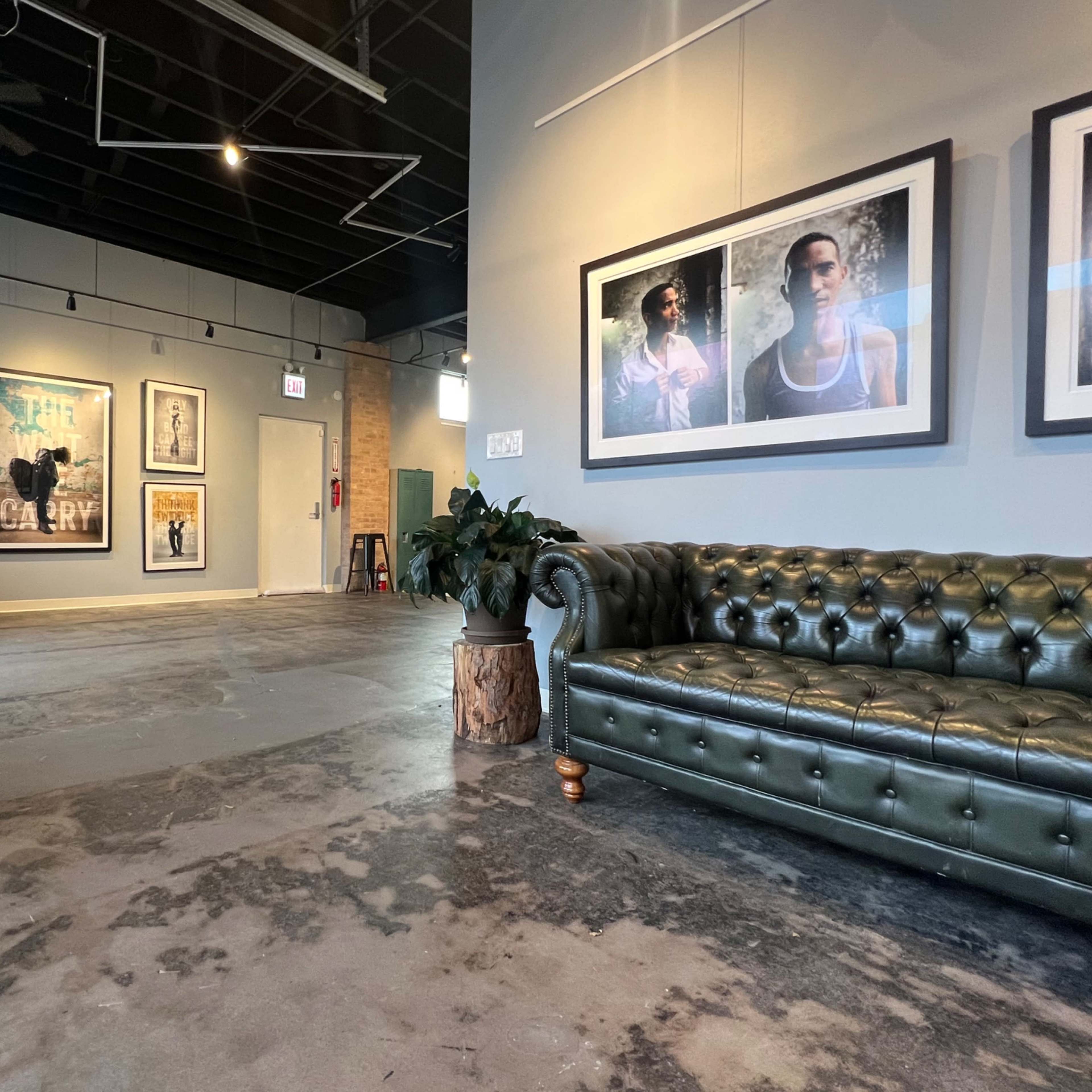 A spacious interior with a green leather sofa, a decorative plant, framed artwork on the wall, and a dark table in the background.
