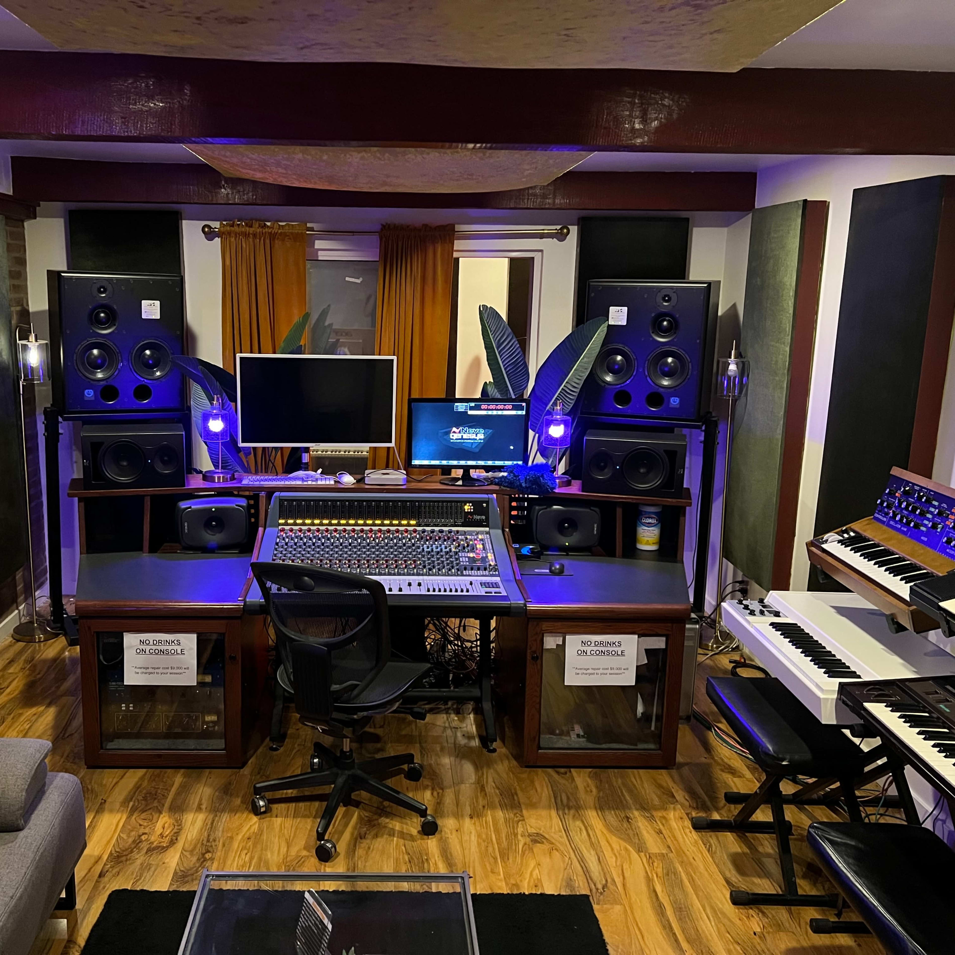 A modern recording studio featuring a large mixing console, multiple speakers, computers, and various musical instruments arranged in a well-furnished space.