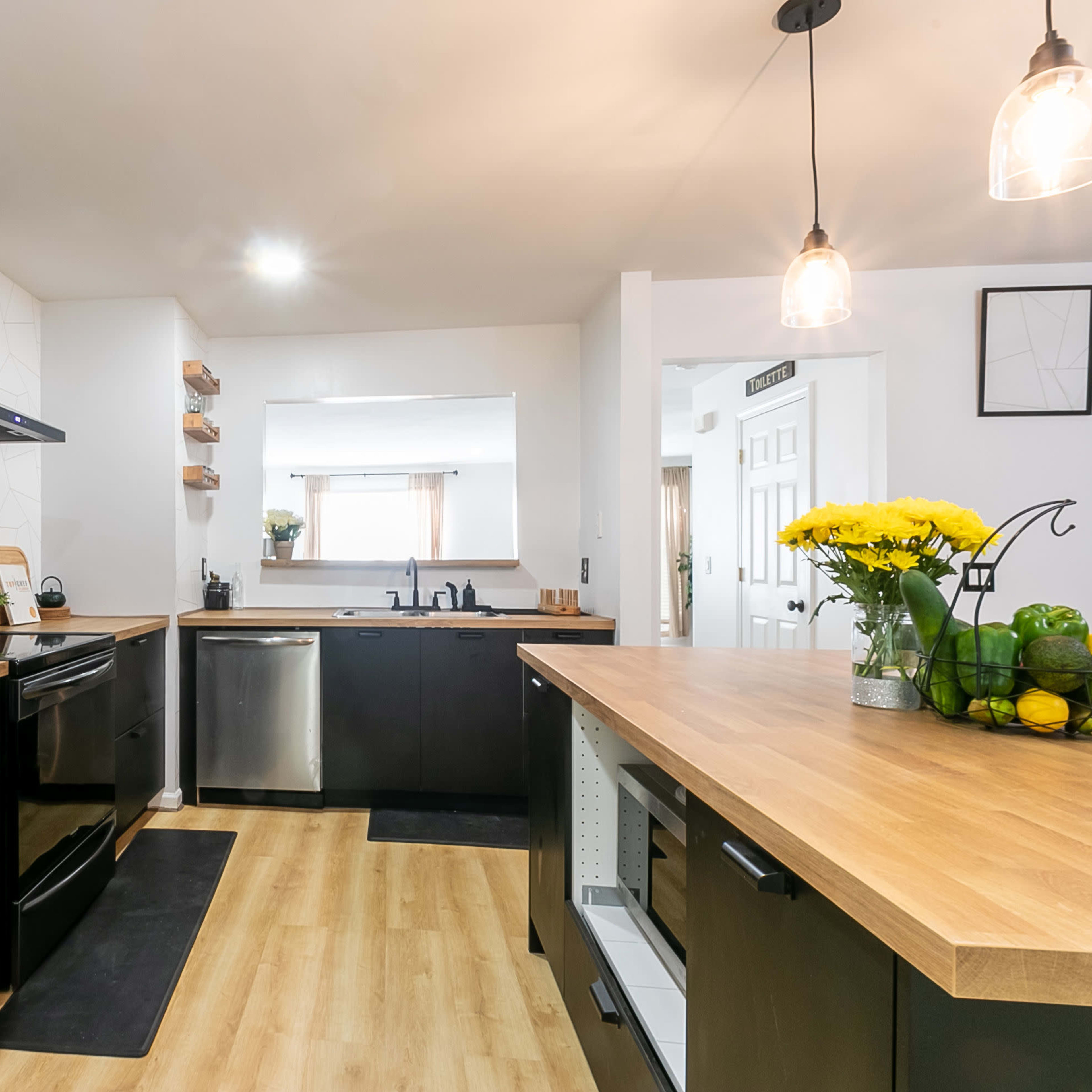 A modern kitchen features stainless steel appliances, wooden countertops, and open shelving with decorative plants.