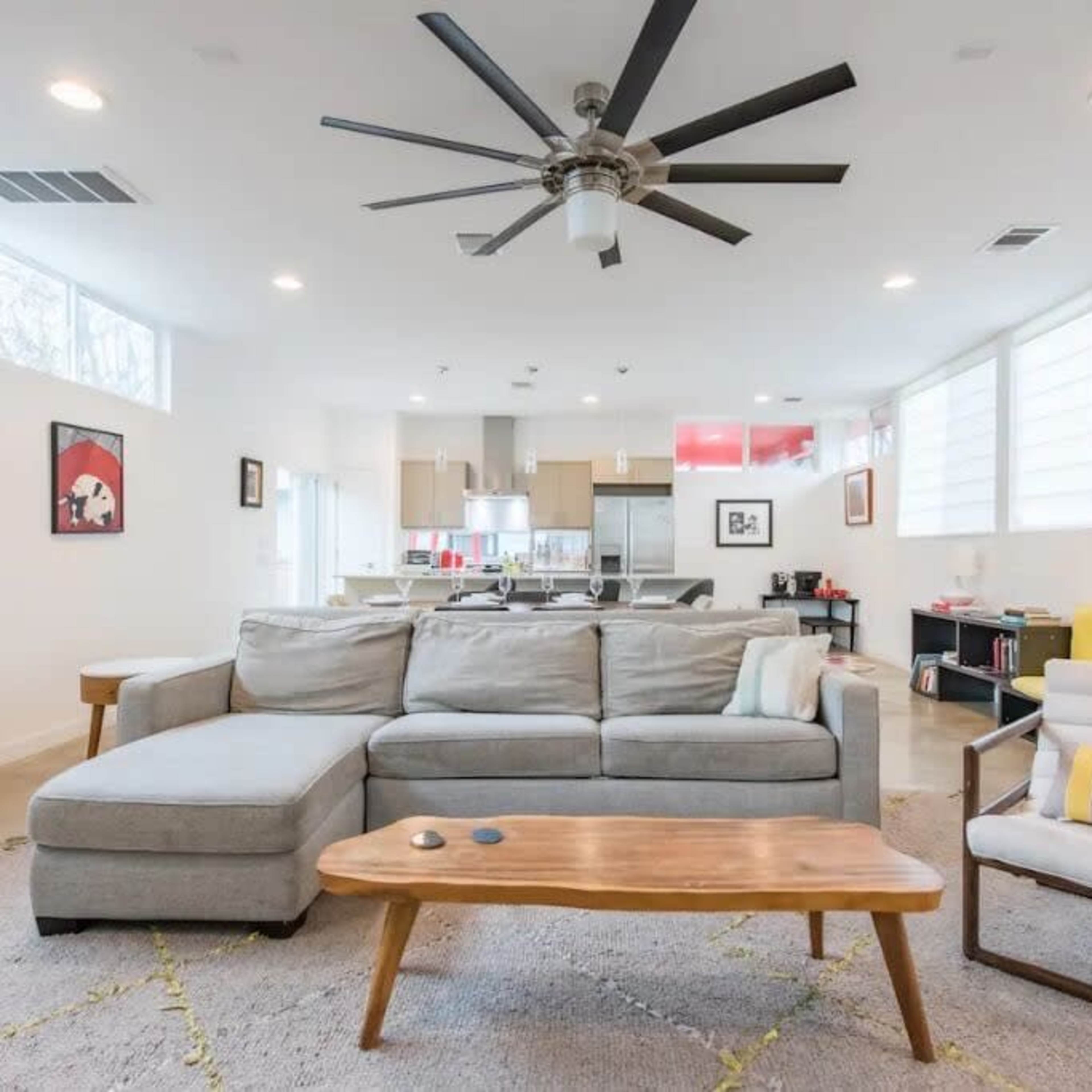 A modern living room features a gray sectional sofa, a wooden coffee table, and large windows with natural light illuminating the space.