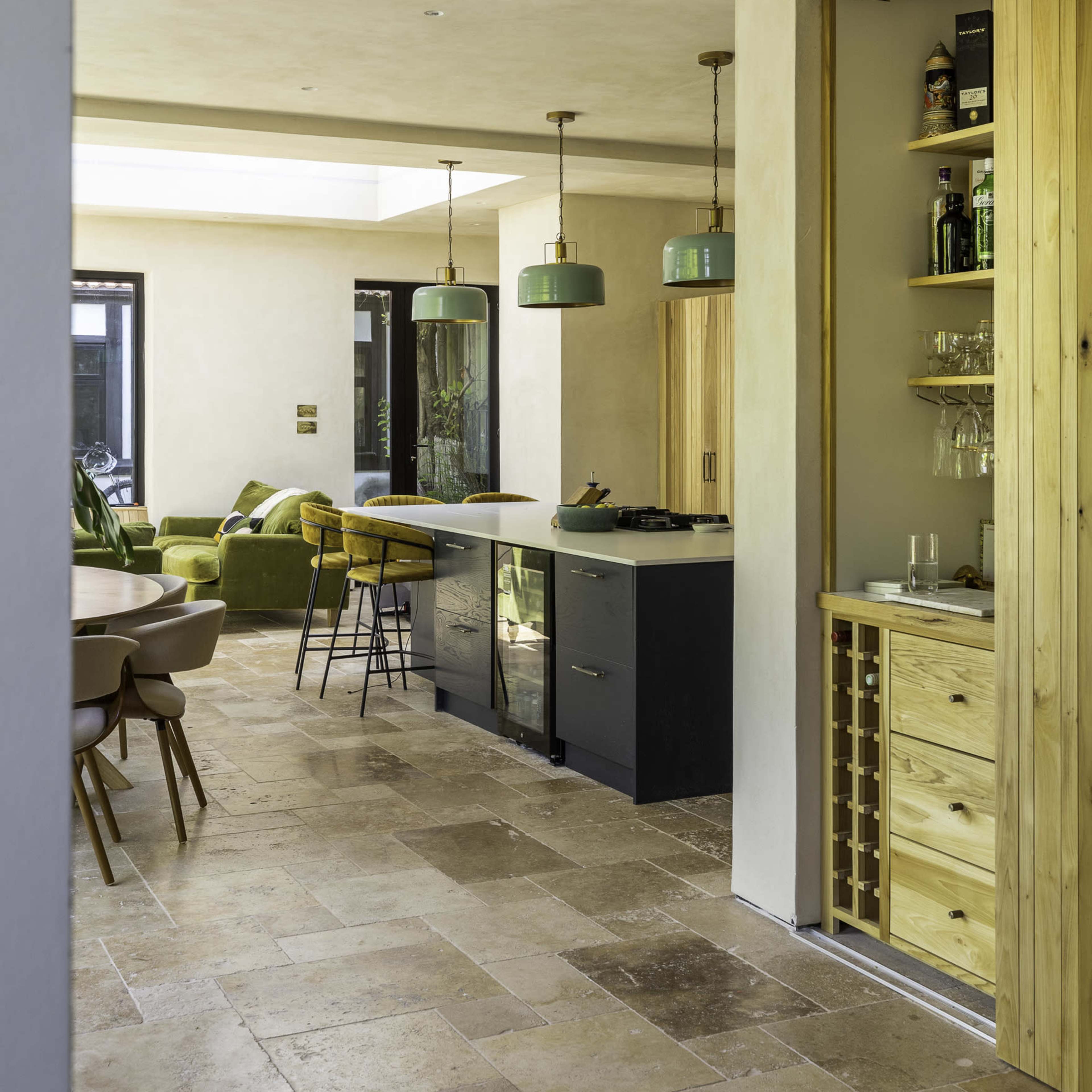 A modern kitchen with earthy tones features a central island, wooden cabinetry, pendant lights, and a dining area with a table and chairs.