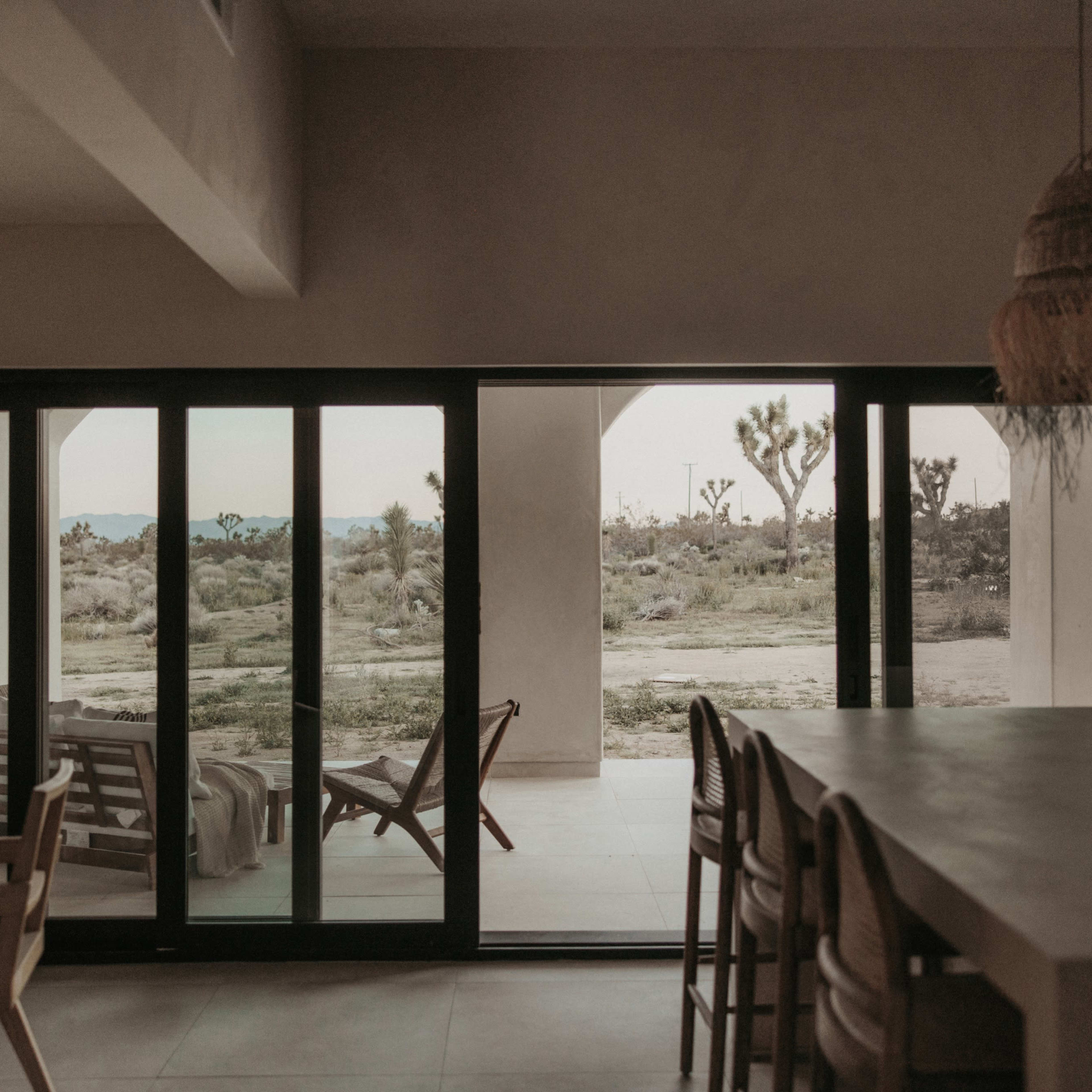A spacious, modern interior with large glass doors that open to a desert landscape featuring scattered vegetation.