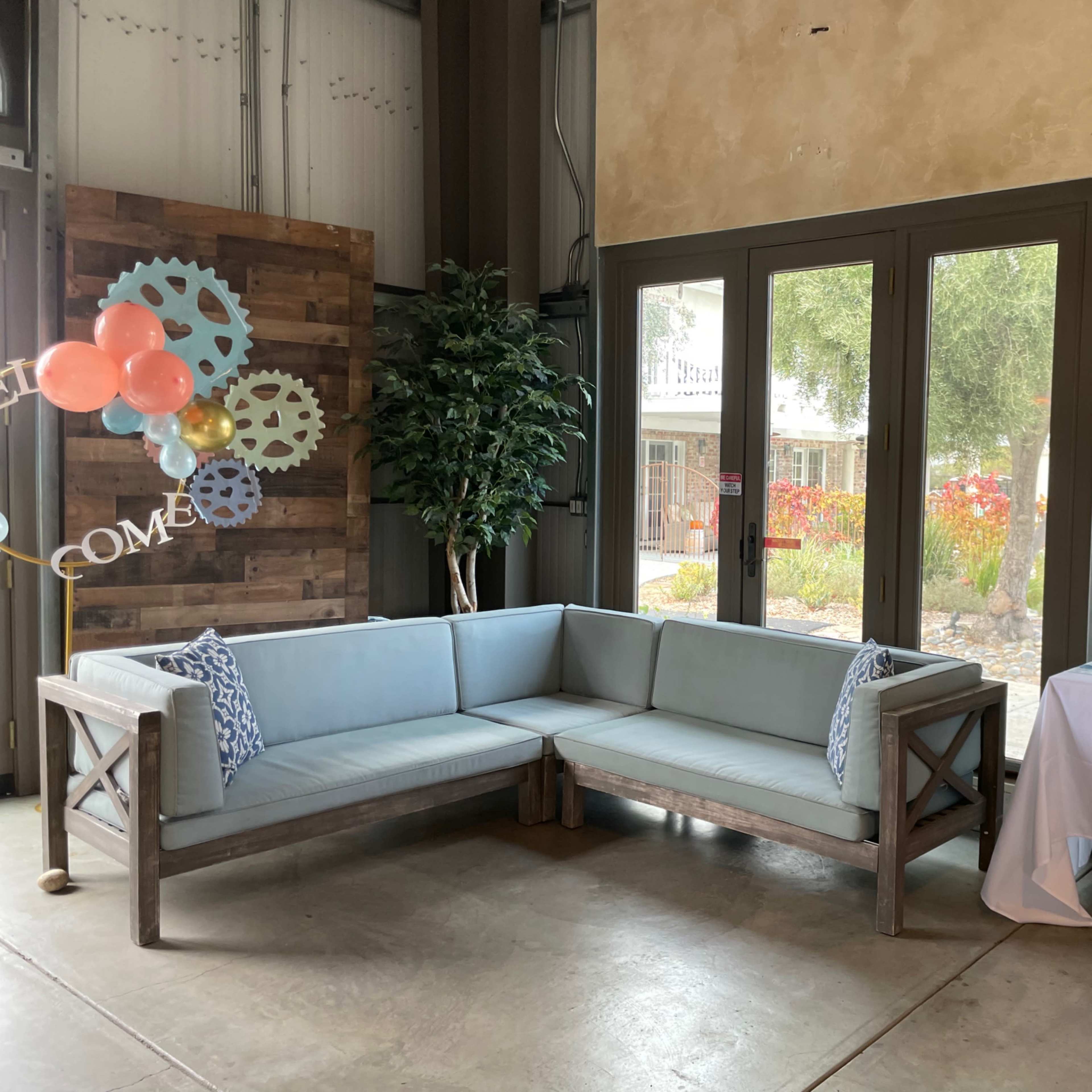 A light blue sectional sofa is positioned beside a table with decorative items and a large window showcasing outdoor greenery.
