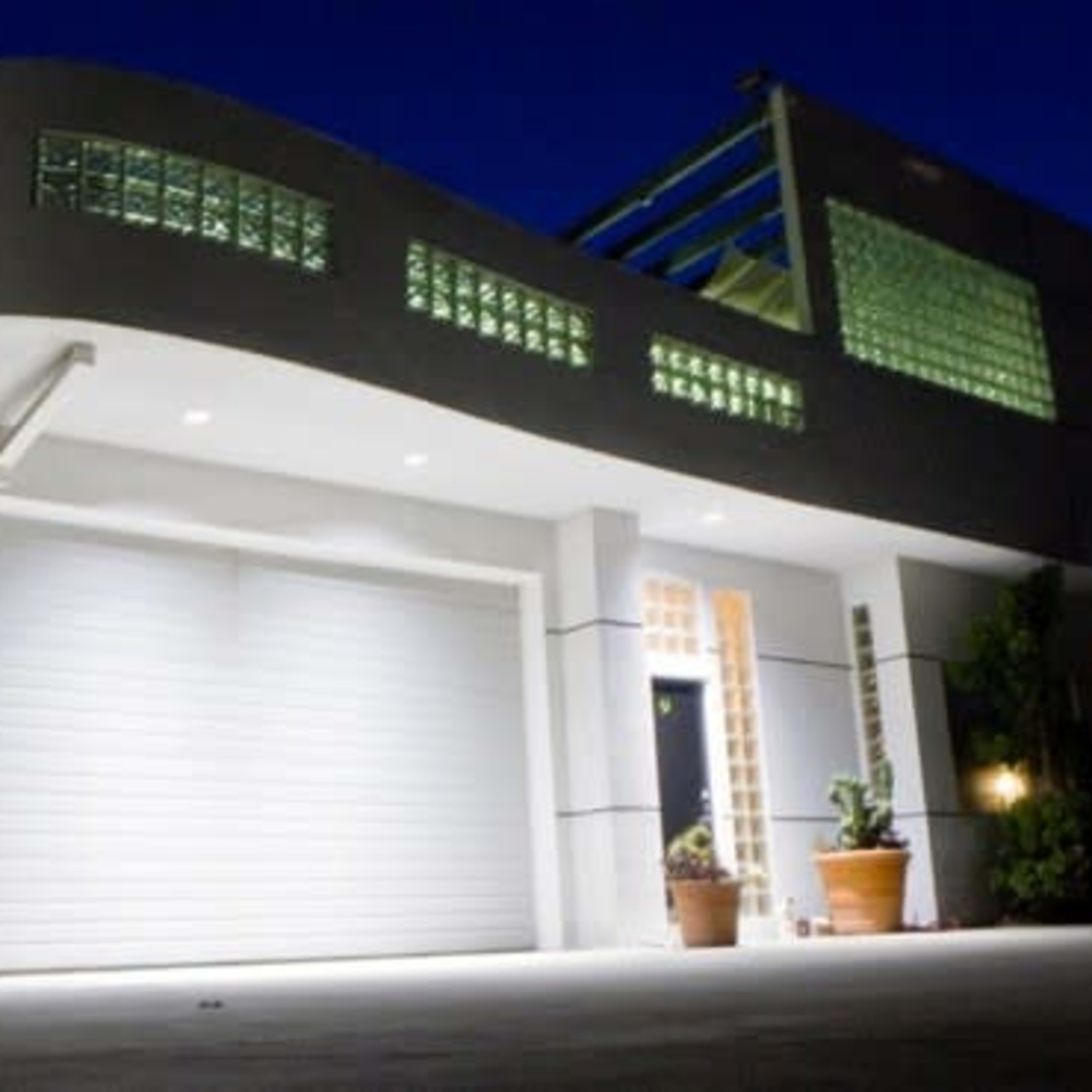 A modern house with a curved roof and glass block windows, illuminated at dusk.