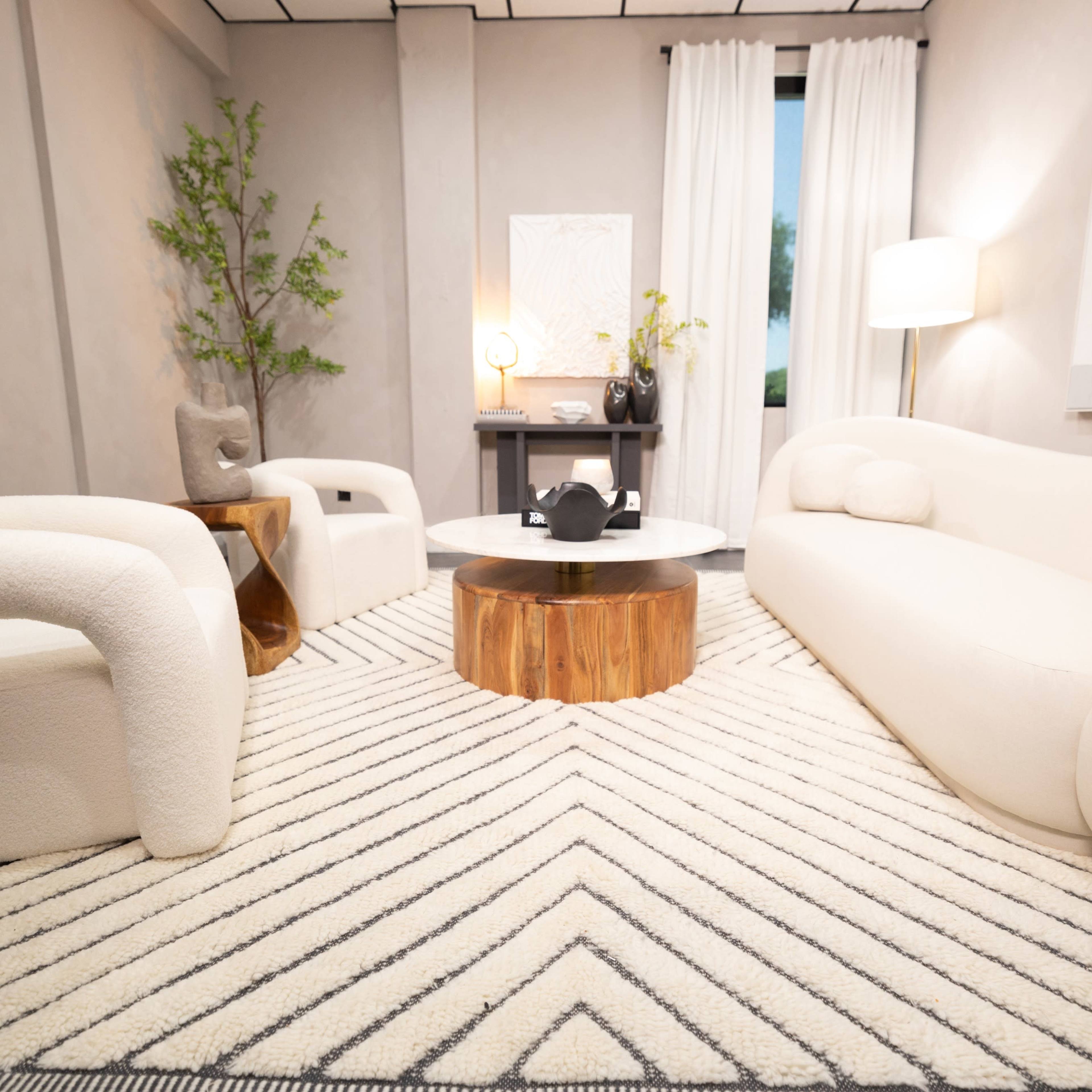 A modern living room with two white sofas, a round wooden coffee table, and a patterned area rug.