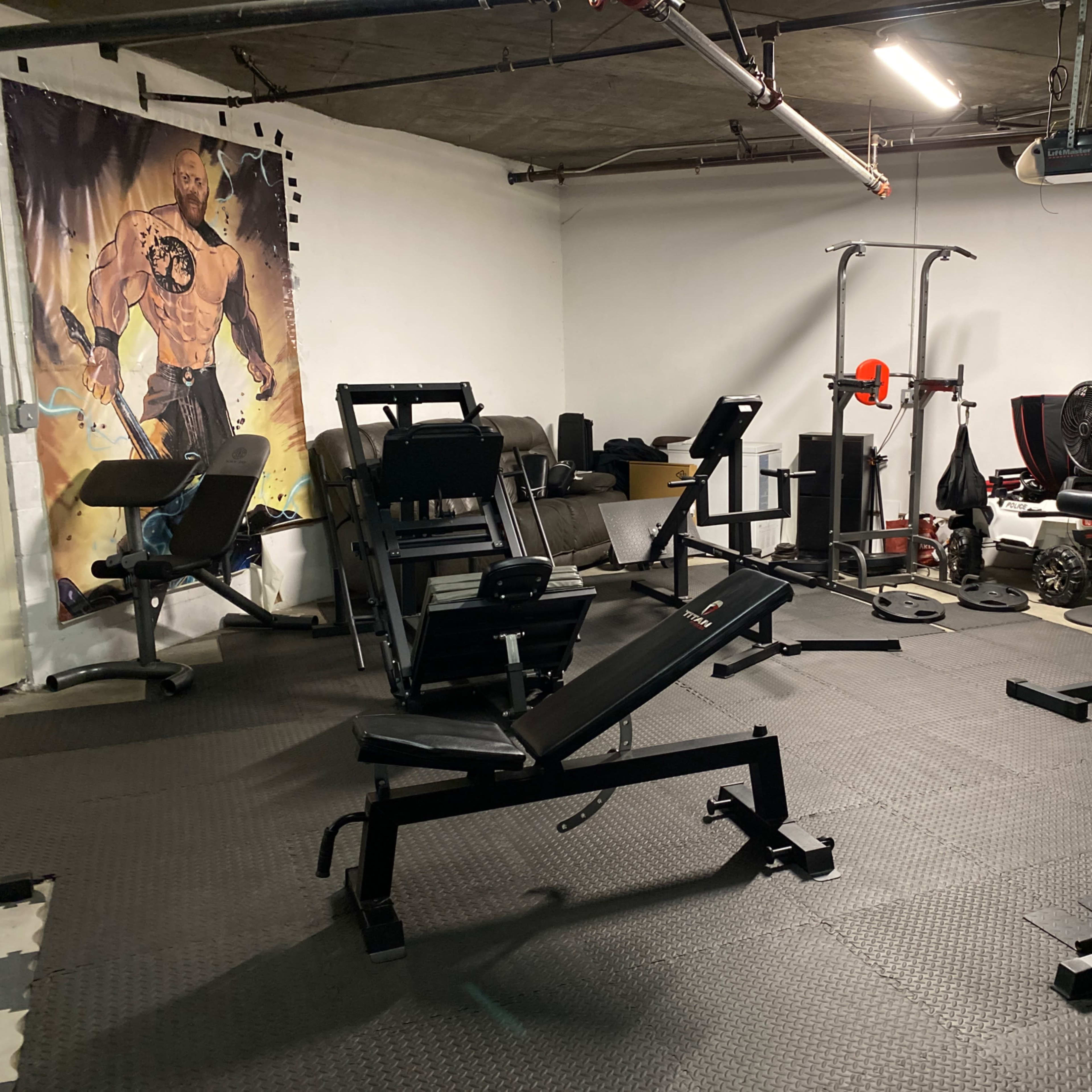 An indoor gym with various workout equipment, including benches, weights, and a wall mural of a muscular figure.