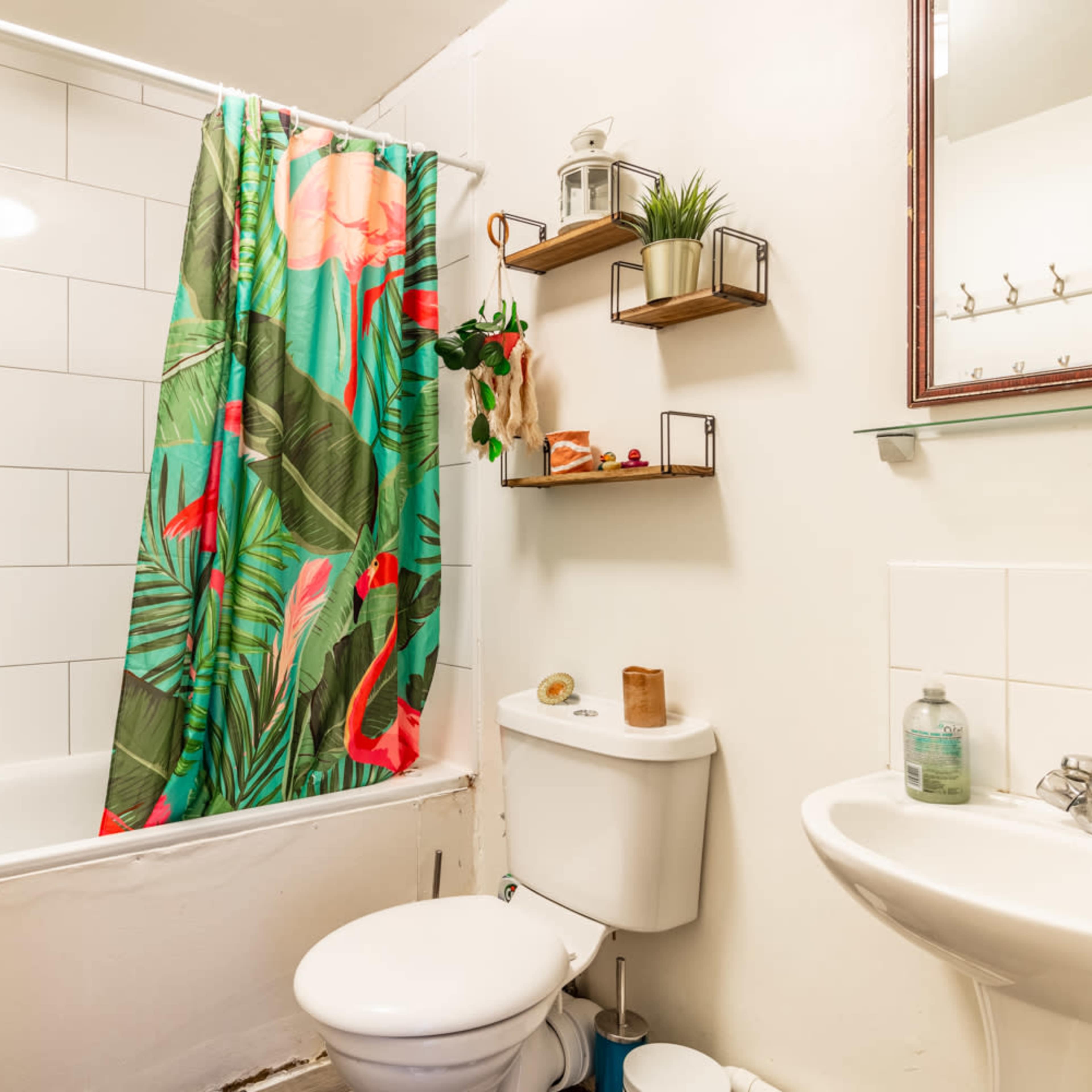 A bathroom featuring a bathtub with a colorful shower curtain, a toilet, a sink, and floating shelves with decorative items.