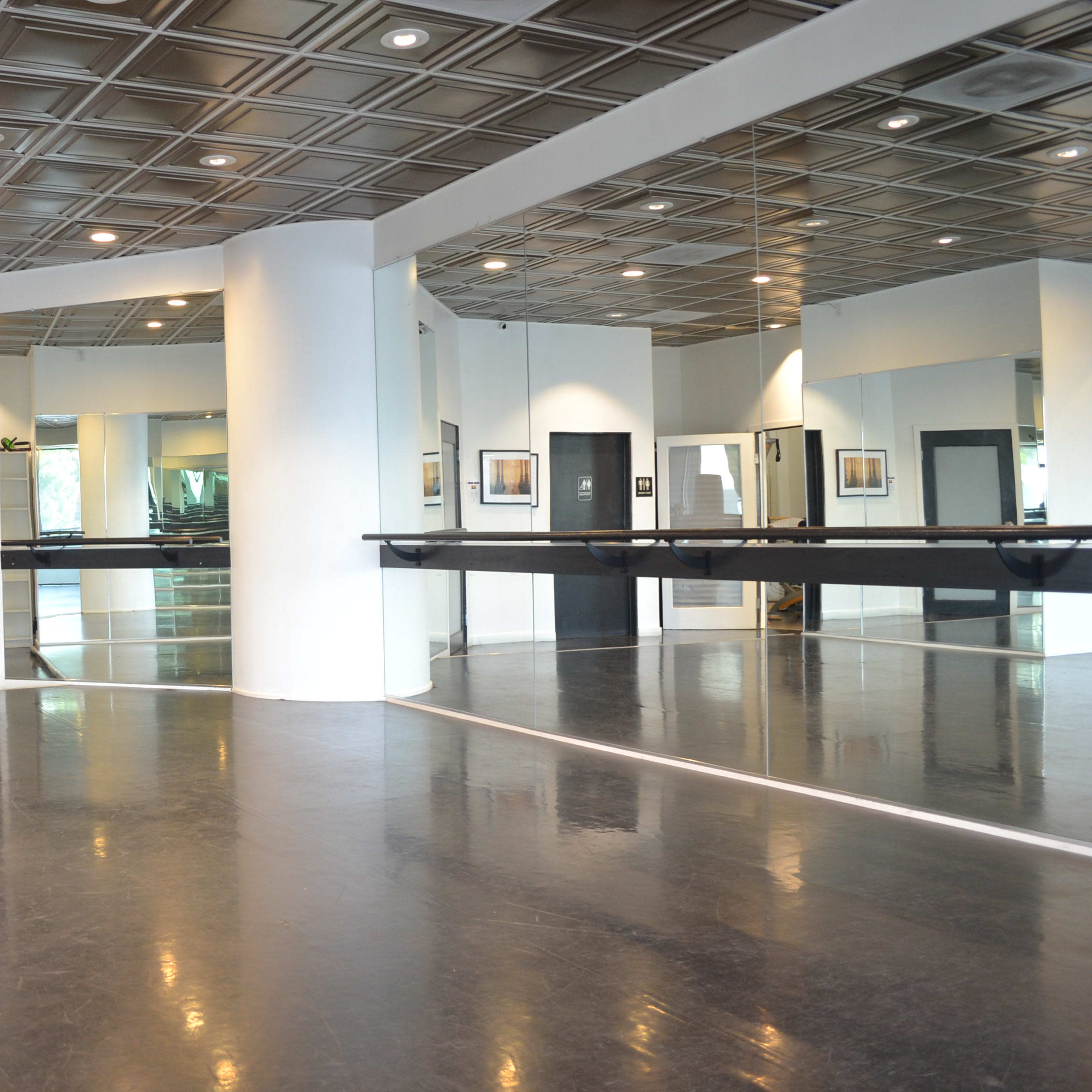 A spacious dance studio with a mirrored wall, polished black floor, and a ceiling with decorative tiles.