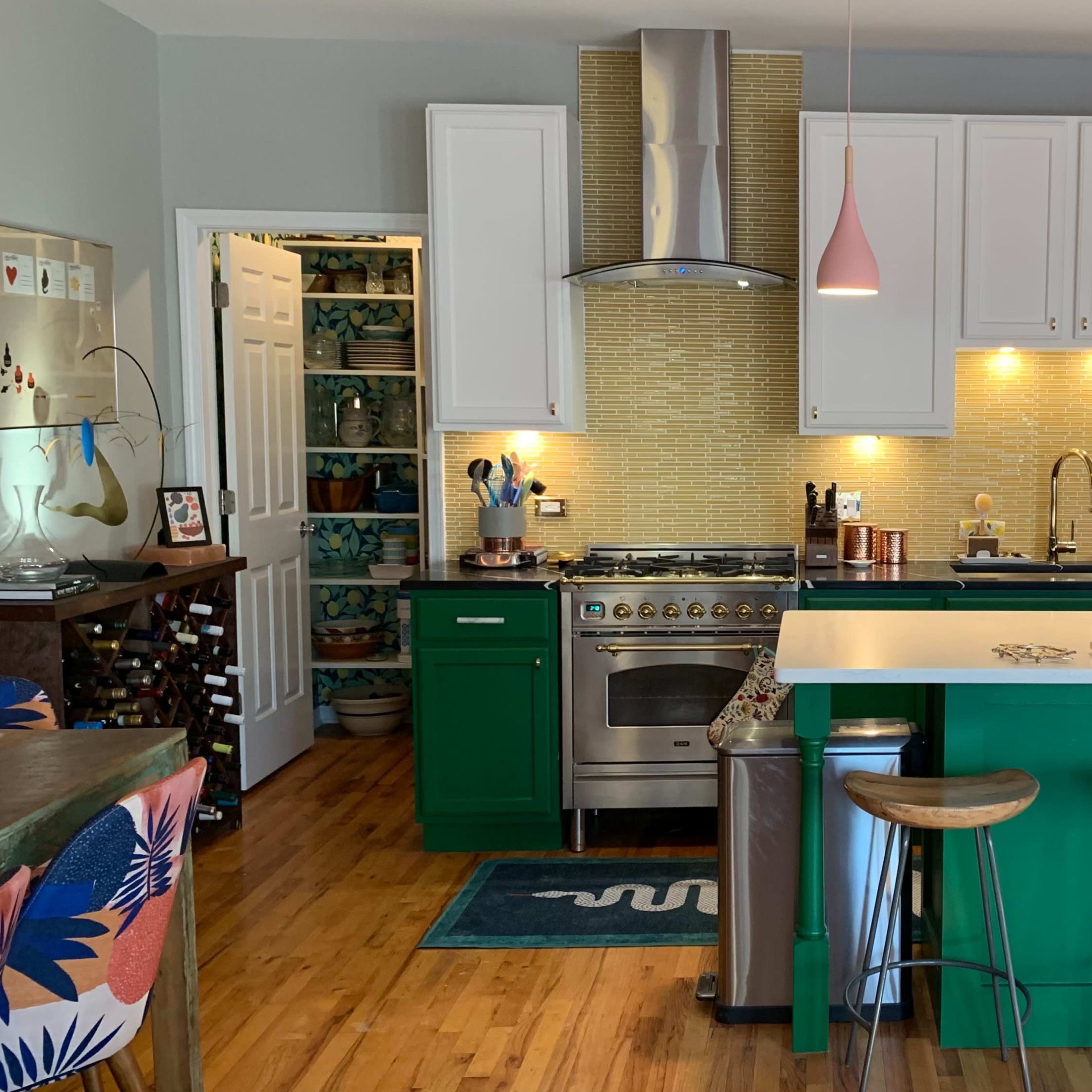 The kitchen features green cabinets, a white island with bar stools, and modern appliances, complemented by a mosaic backsplash and pendant lights.