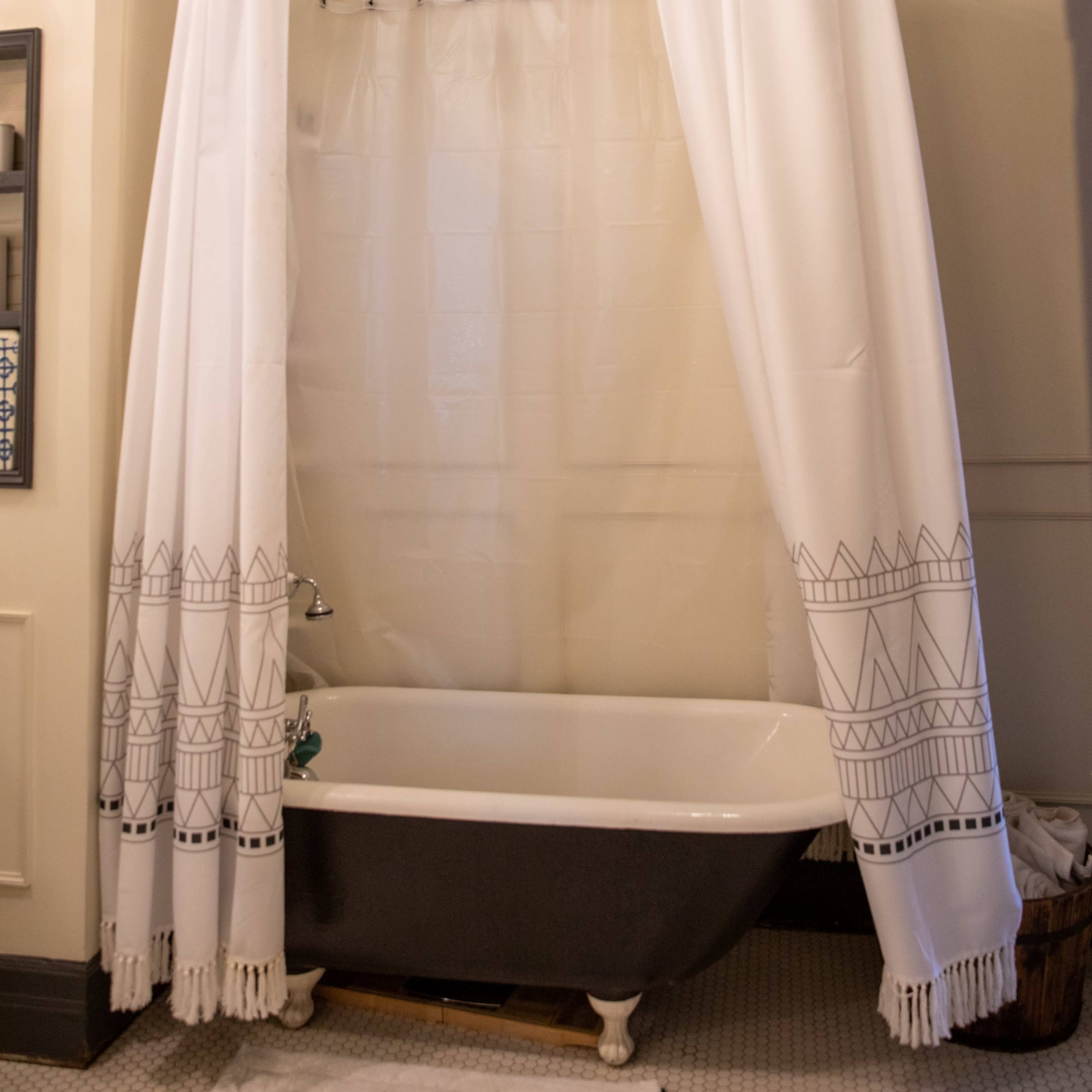 A clawfoot bathtub is enclosed by white curtains and a chandelier hangs above in a bathroom with light-colored walls.