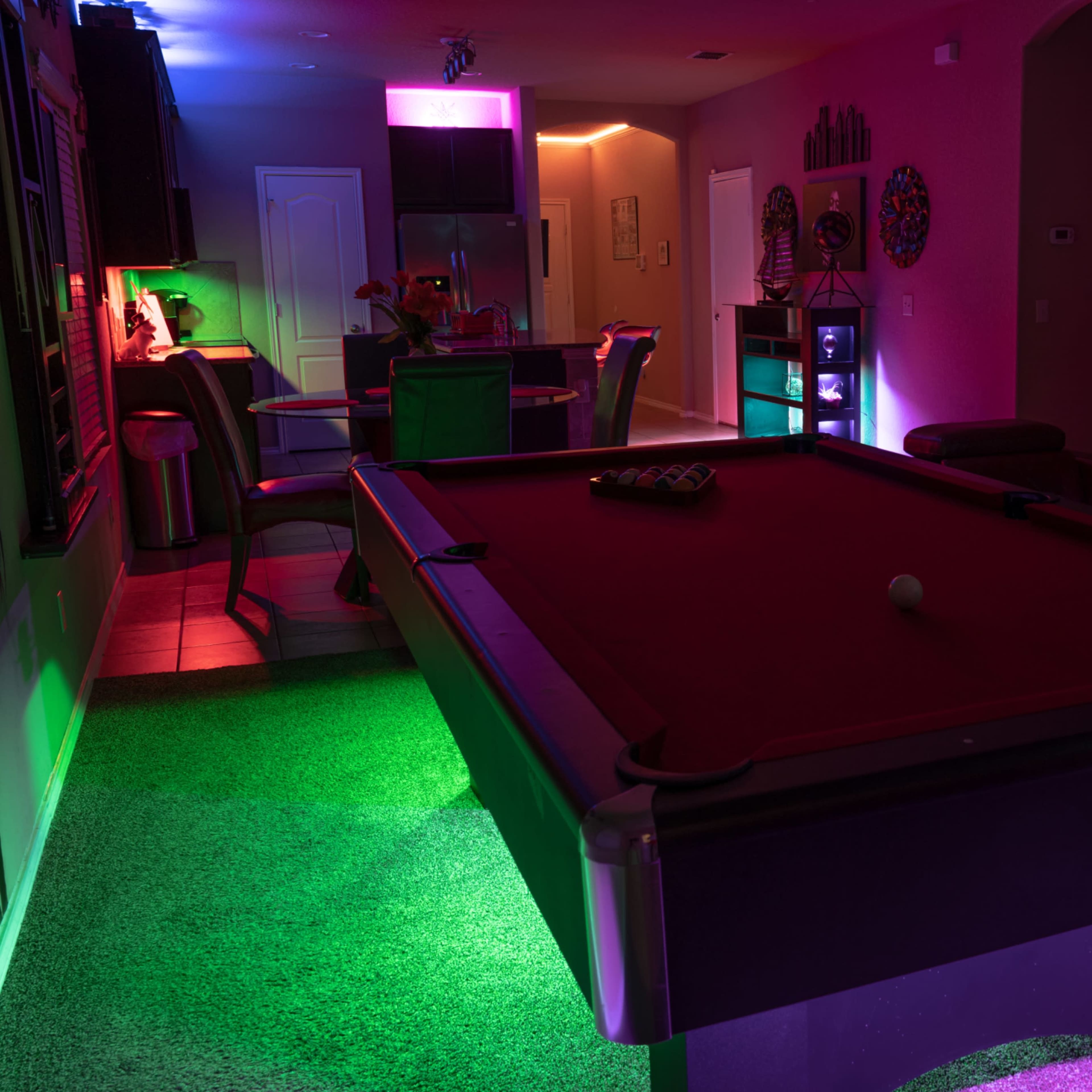 A dimly lit game room featuring a billiards table and vibrant colored lighting along the walls and ceiling.