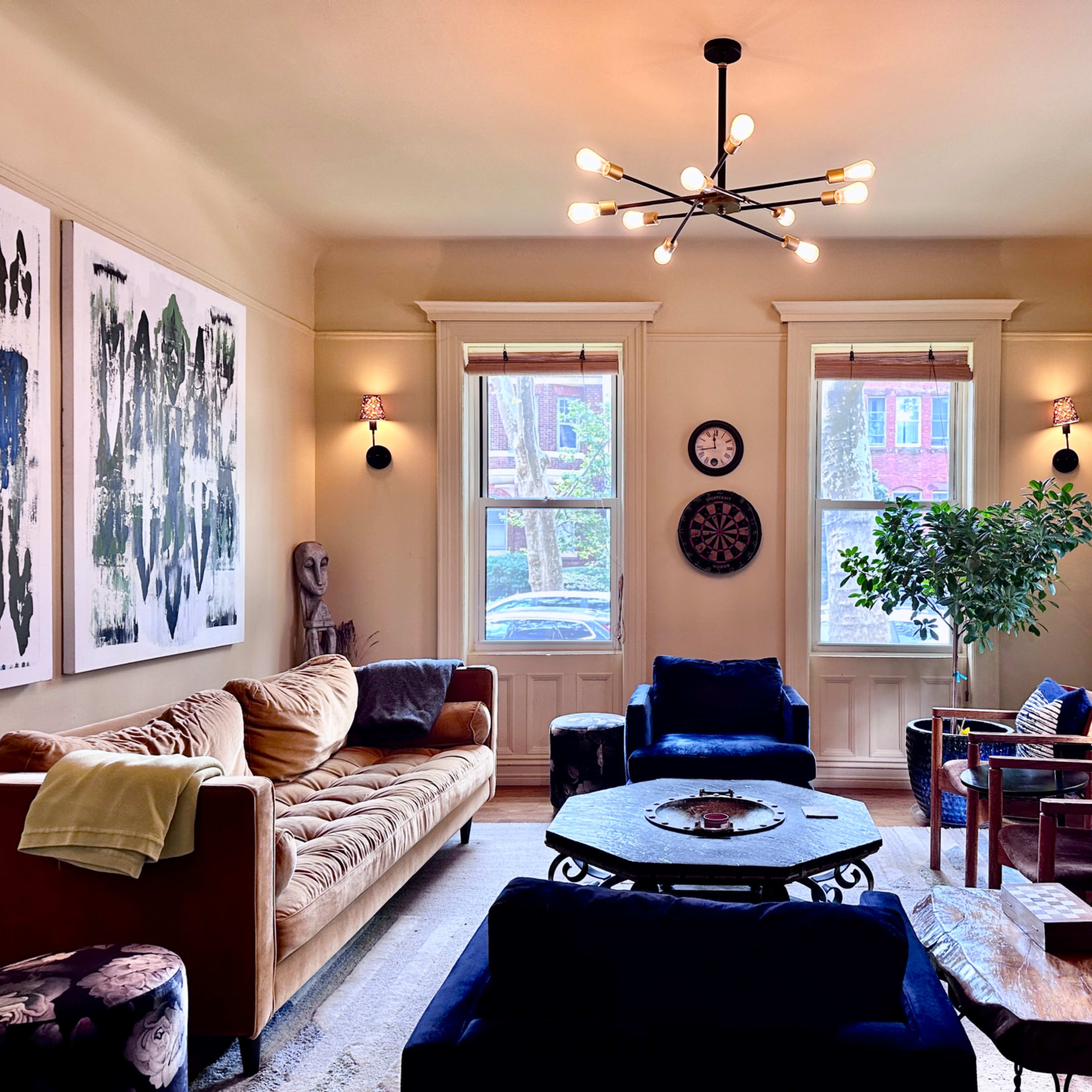 A living room featuring a mix of seating arrangements, art on the walls, and large windows allowing natural light to enter.