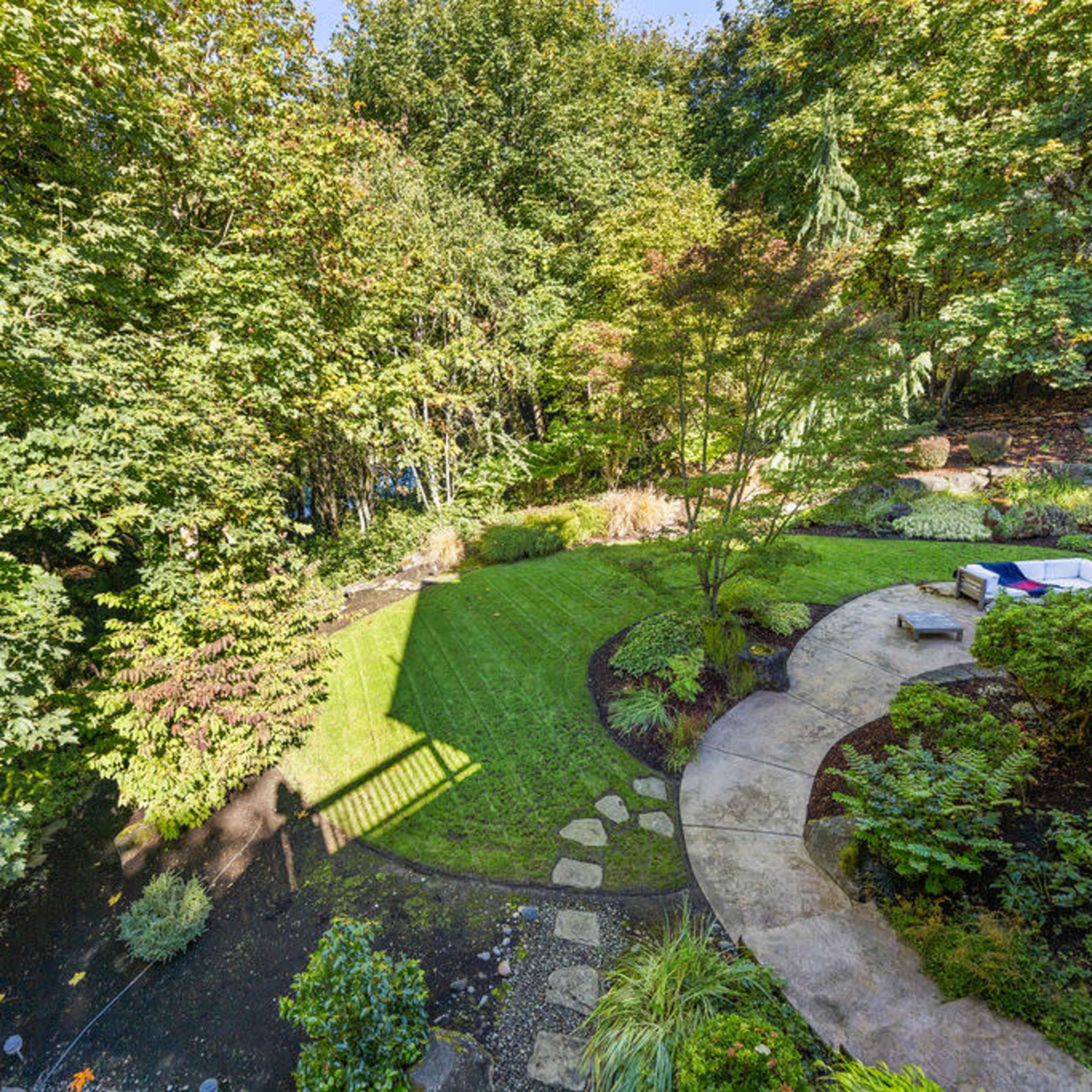 A landscaped backyard with a curved stone pathway, a well-manicured lawn, and dense trees in the background.