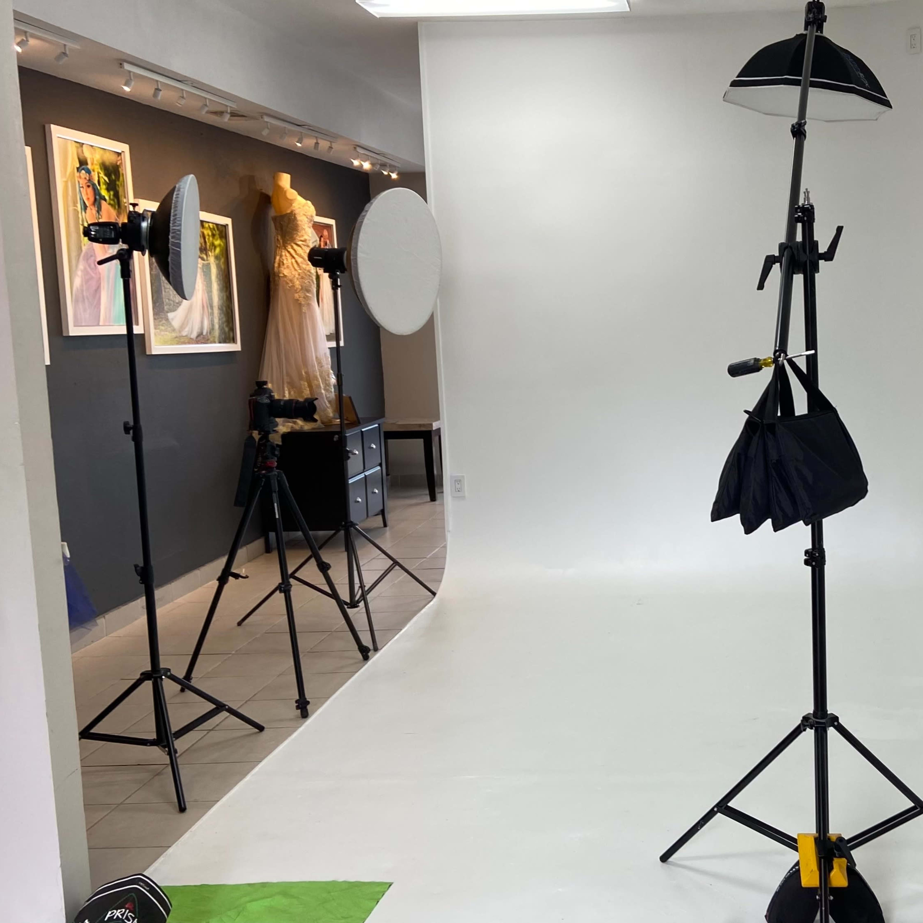 A photography studio with a blank white backdrop, softbox lights, and a tripod stand holding a reflector.