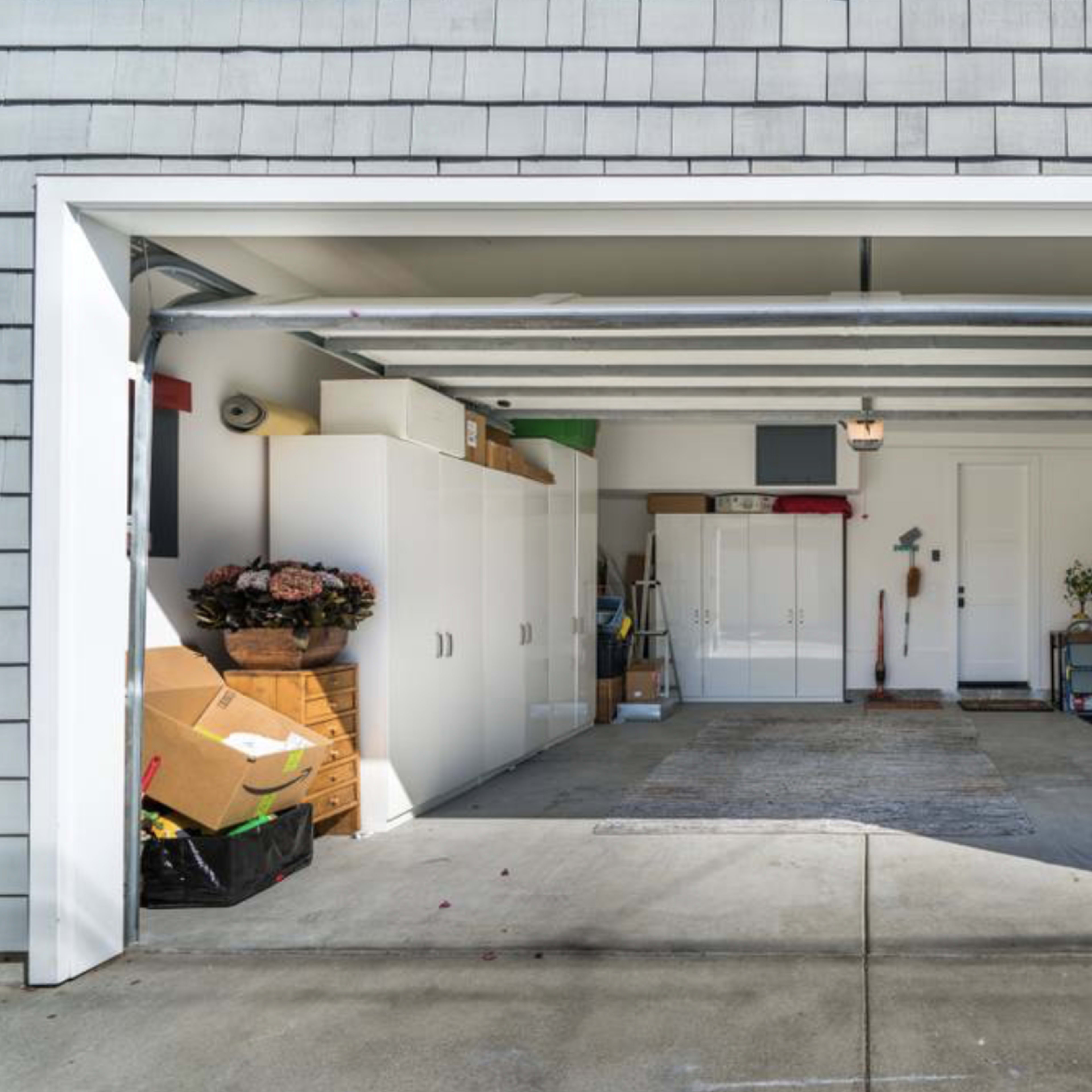 A garage features neatly stored boxes and cabinets along one side, with a concrete floor and a rug positioned at the entrance.