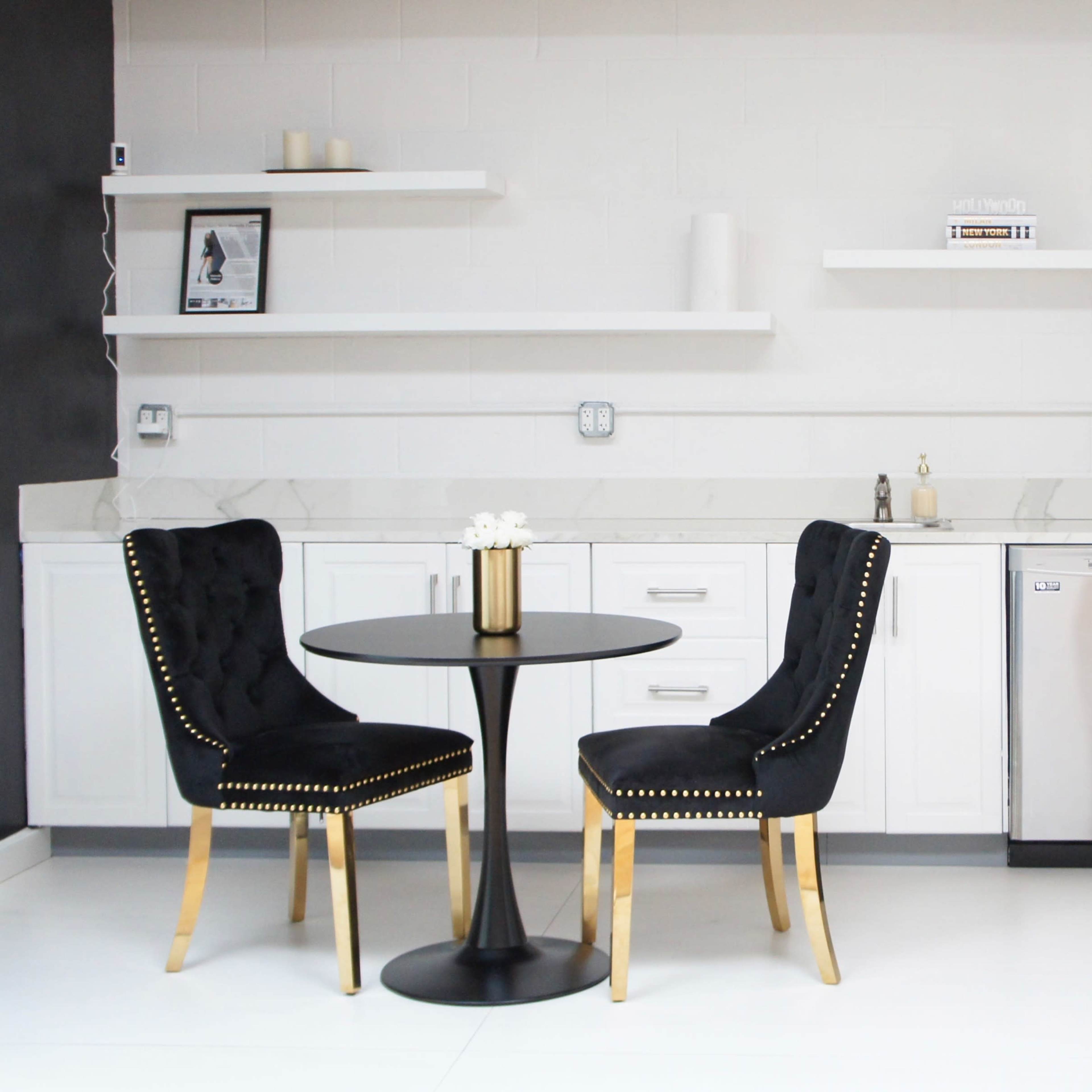 A modern kitchen features a round black table with two chairs and stainless steel appliances, including a refrigerator and dishwasher.