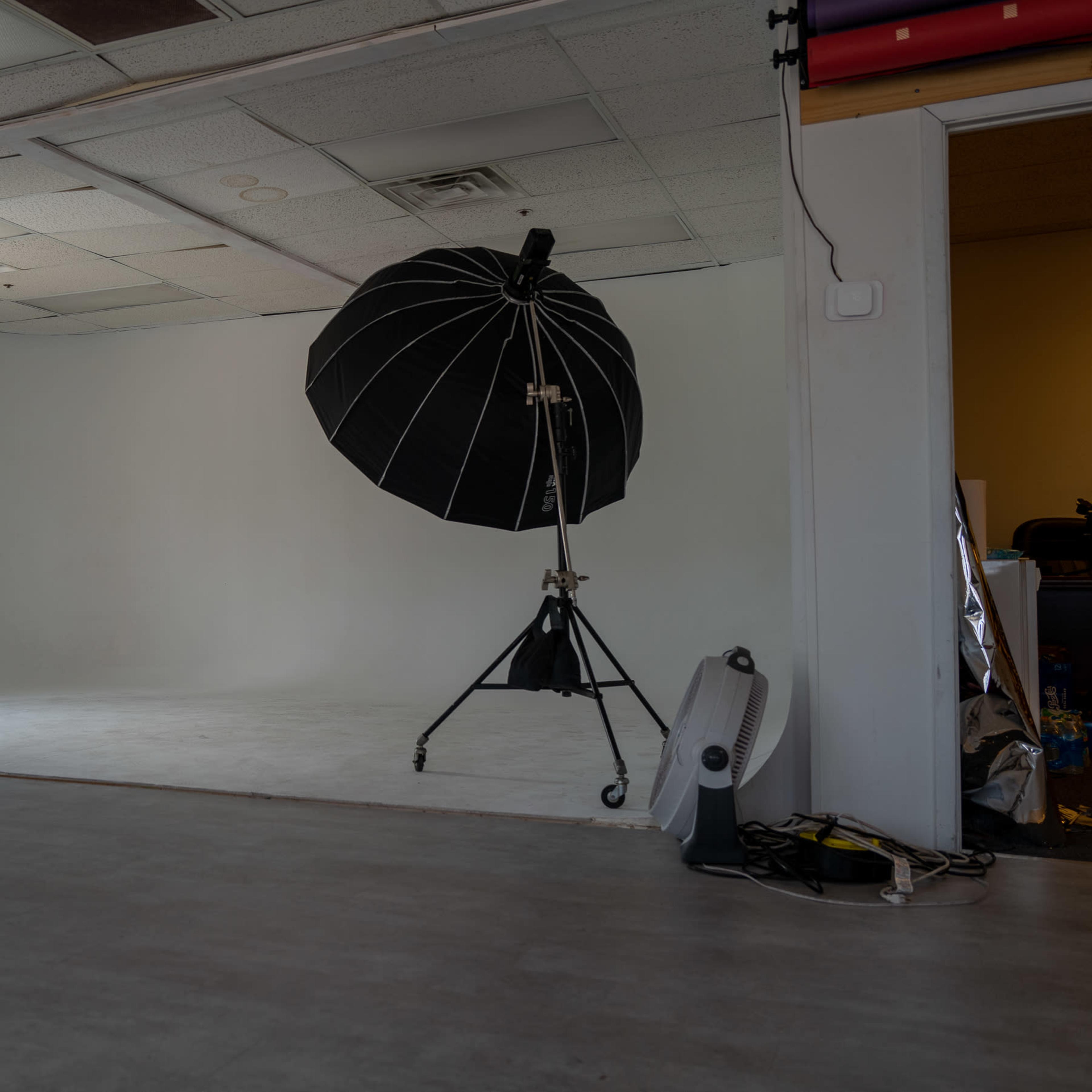 A spacious photography studio with a large black umbrella light on a stand, white walls, and a light-colored floor.