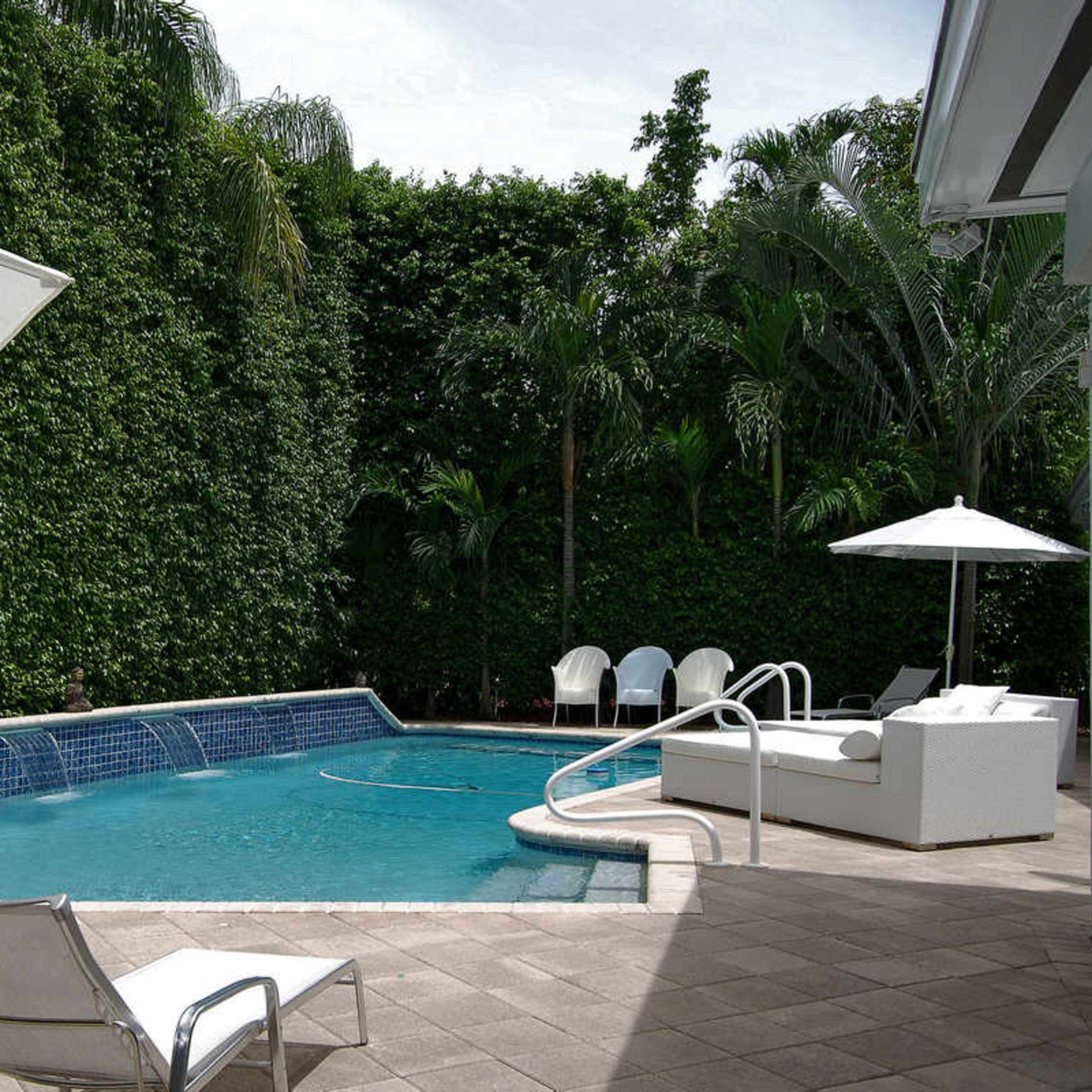 A swimming pool surrounded by lush greenery, with lounge chairs and umbrellas nearby.