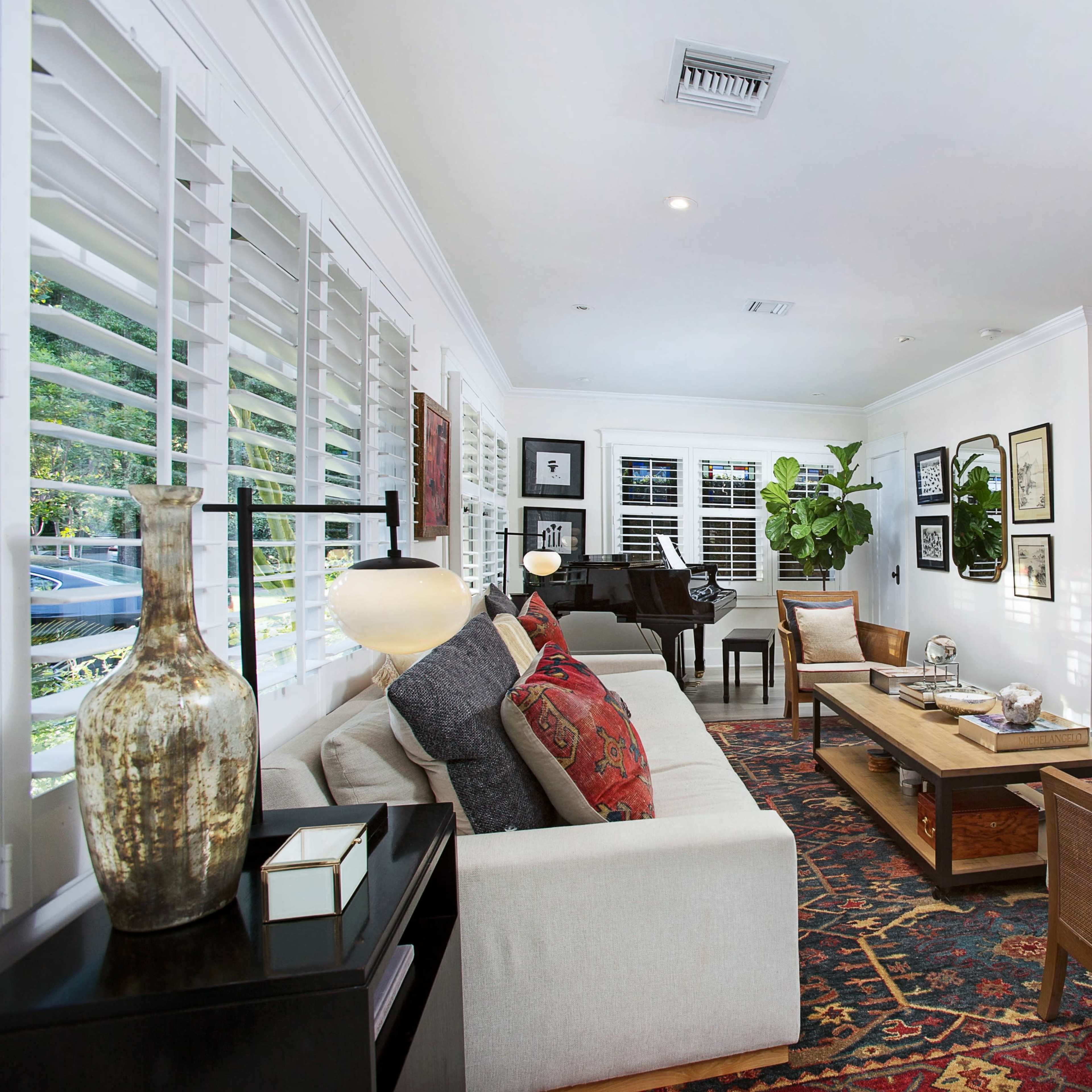 A cozy living room with a sofa, decorative pillows, a coffee table, and a television mounted on the wall, surrounded by framed artwork and plants.