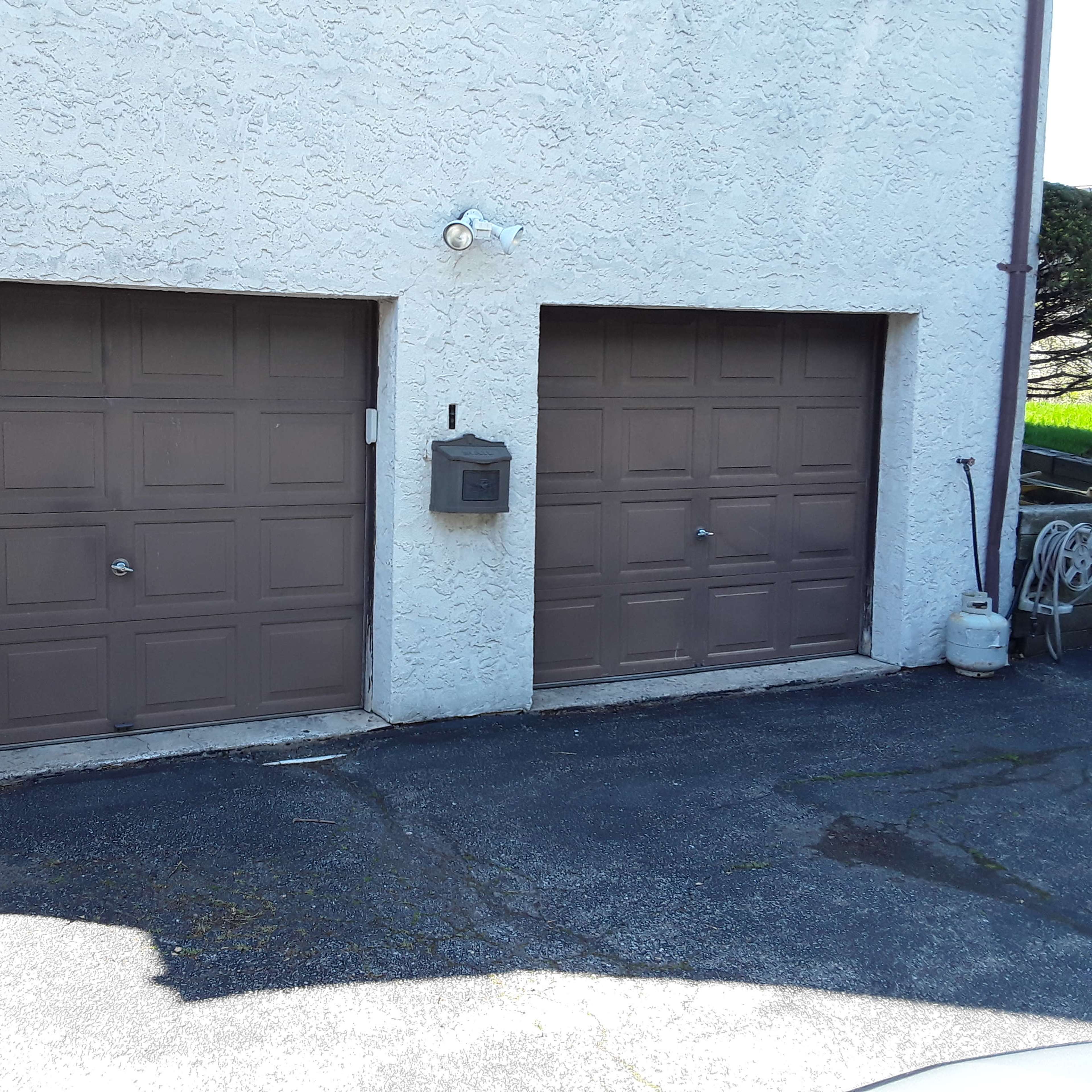 Two closed brown garage doors next to each other on a textured light-colored wall.