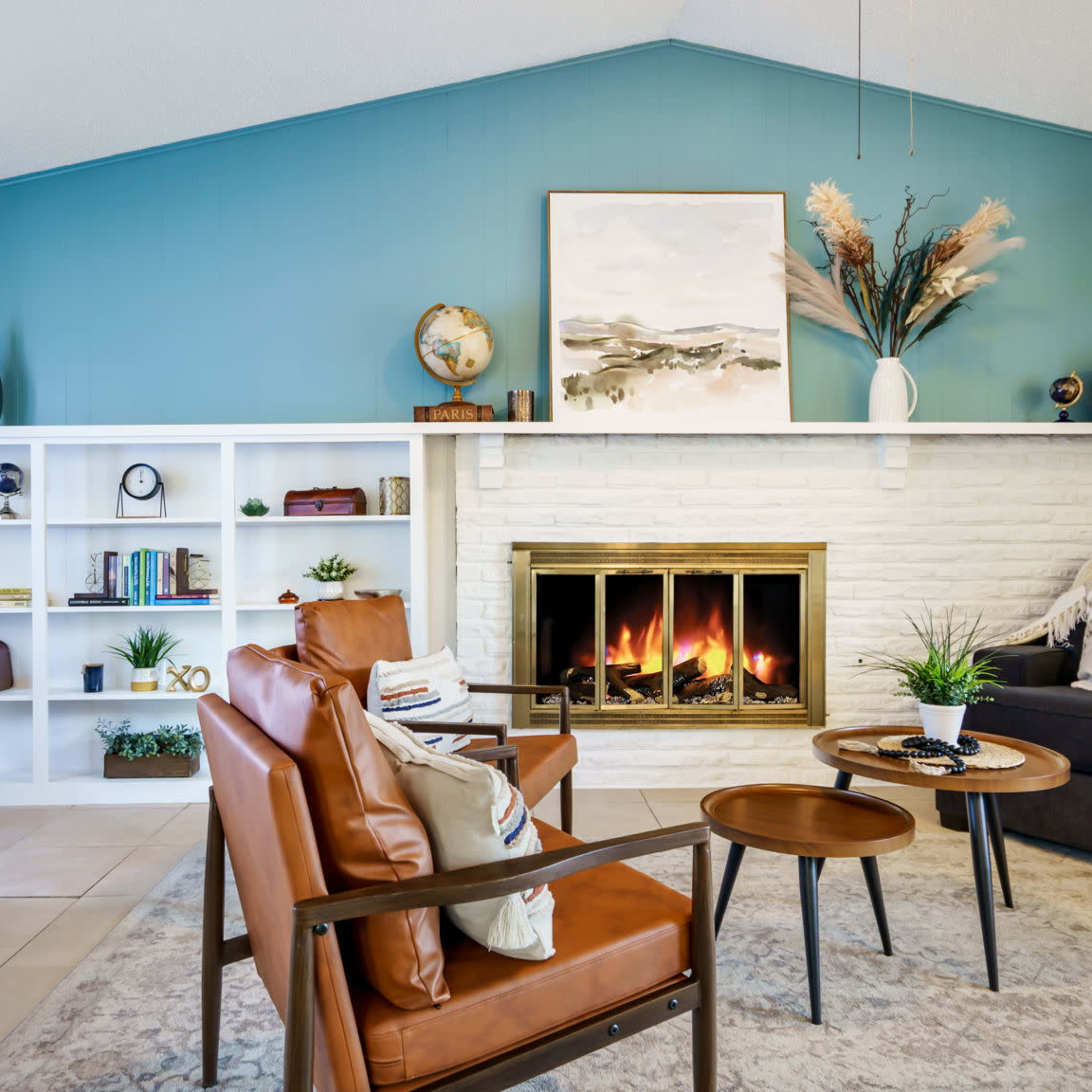 A bright living room features a fireplace, a comfortable seating area with leather chairs and a sofa, and shelves filled with books and decorative items.