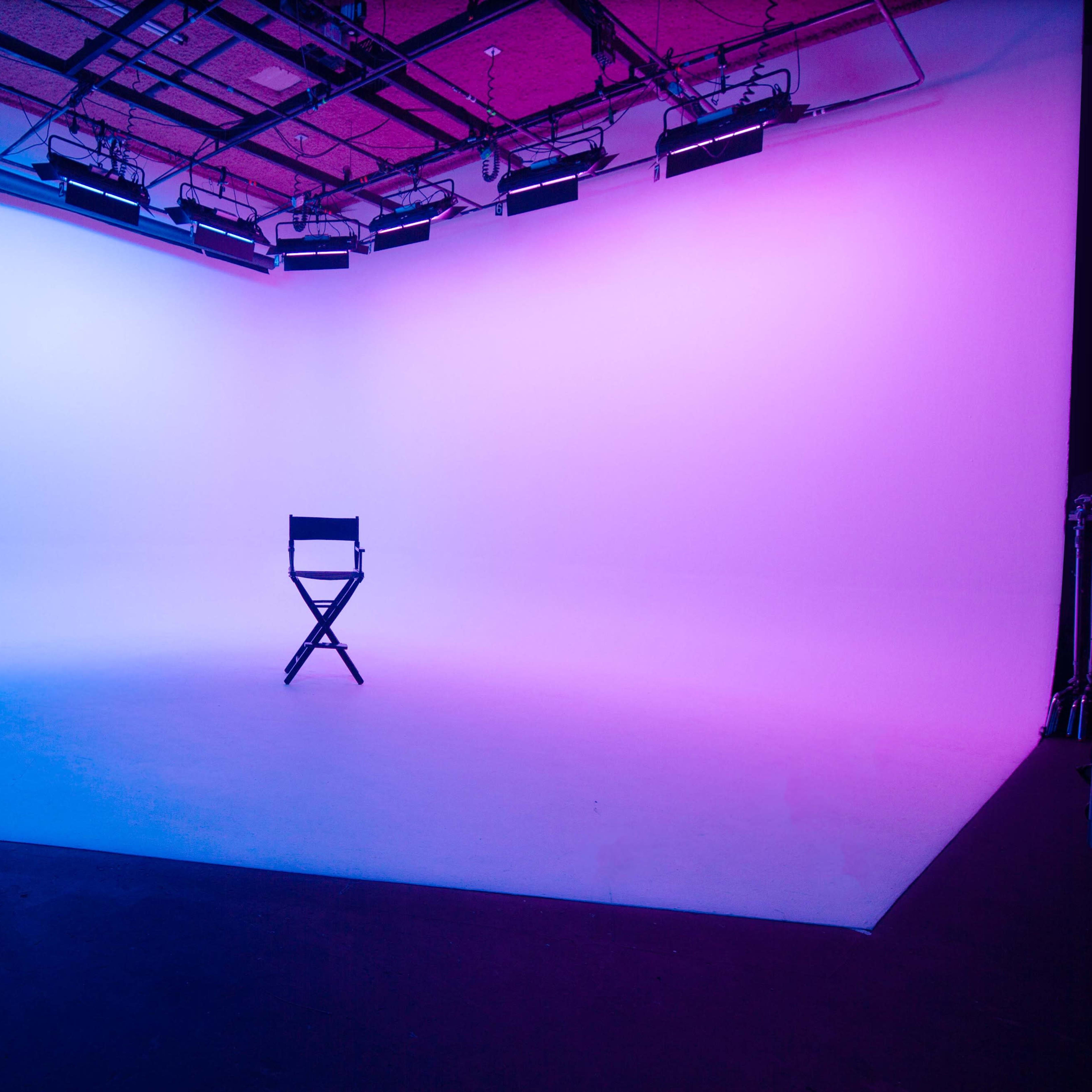 A director's chair is placed in the center of a brightly lit studio with a gradient background of blue and pink.